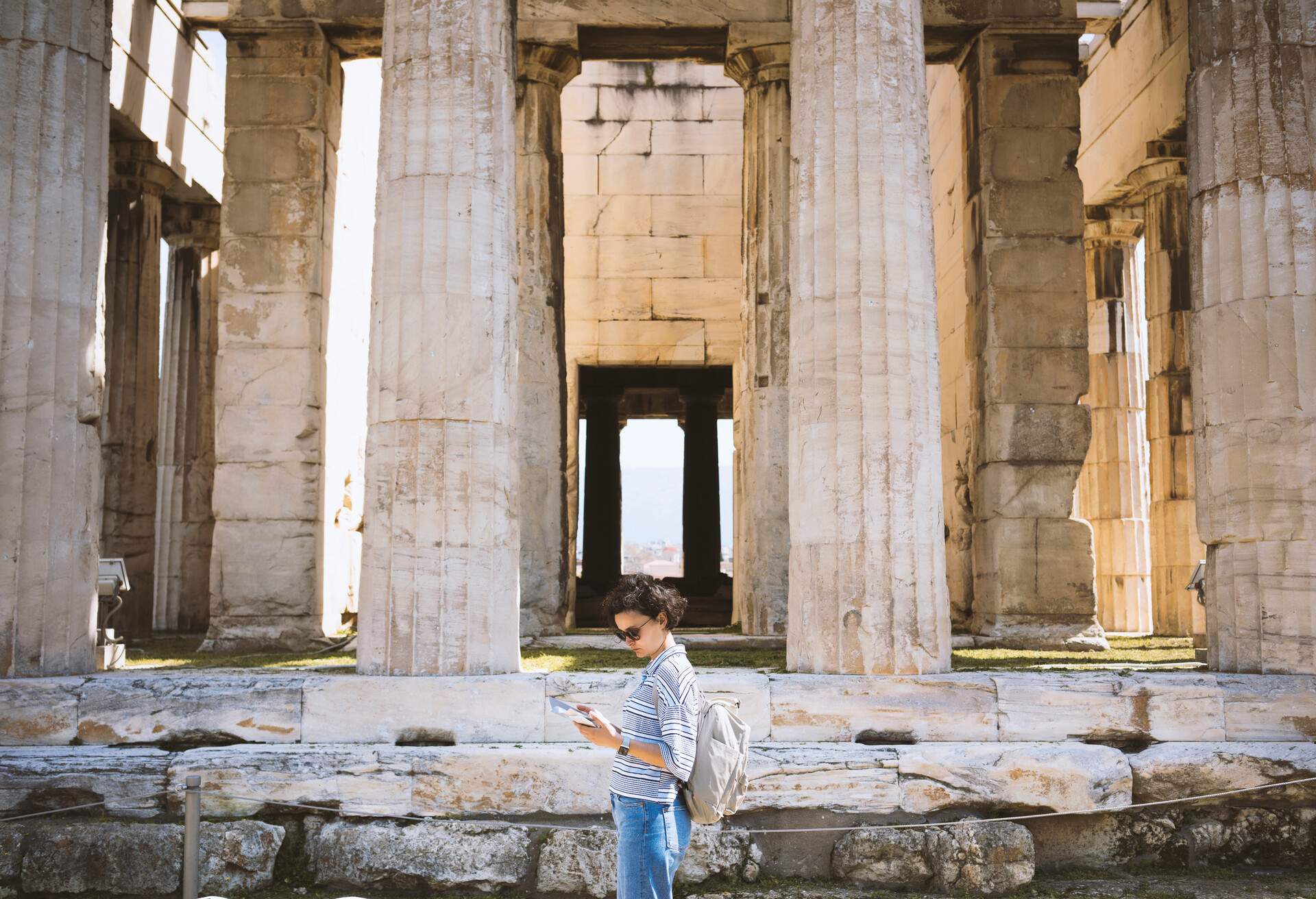 A female tourist reading a pamphlet while standing in front of a Greek temple.