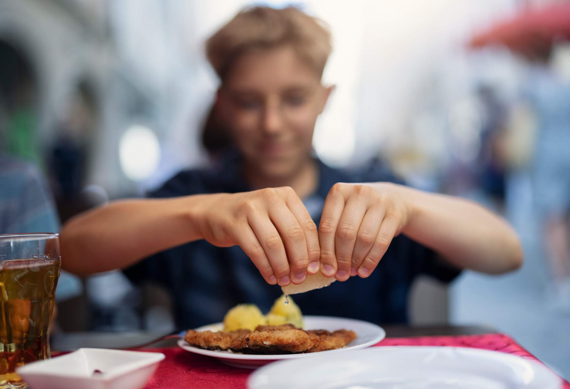 Teenage boy eating wiener schnitzel in a restaurant. The boy is squeezing lemon over the schnitzel...Nikon D850