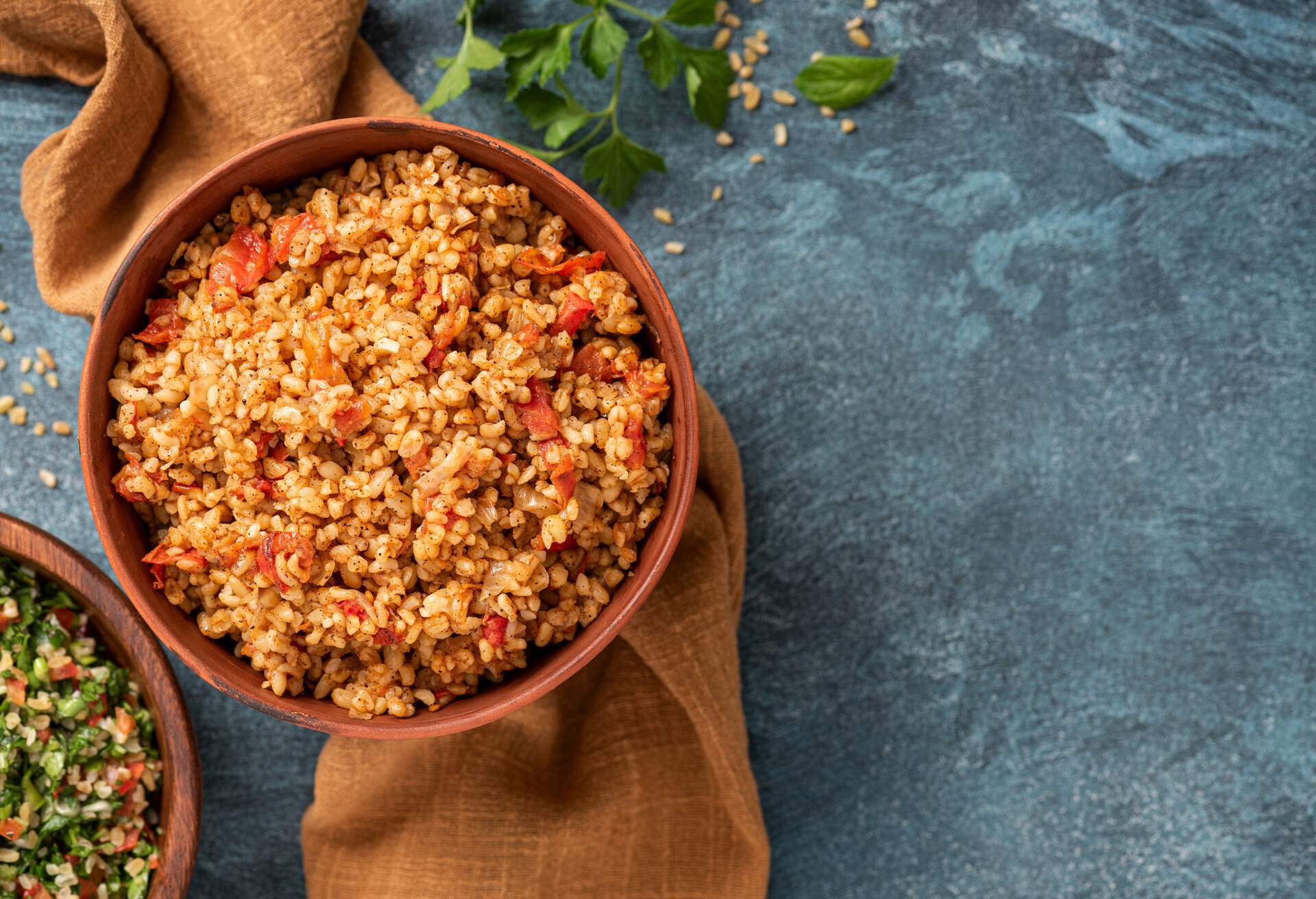 Easy bulgur pilaf (pilavi) with tomatoes in a ceramic bowl on a dark background top view. Turkish cuisine, vegan food.