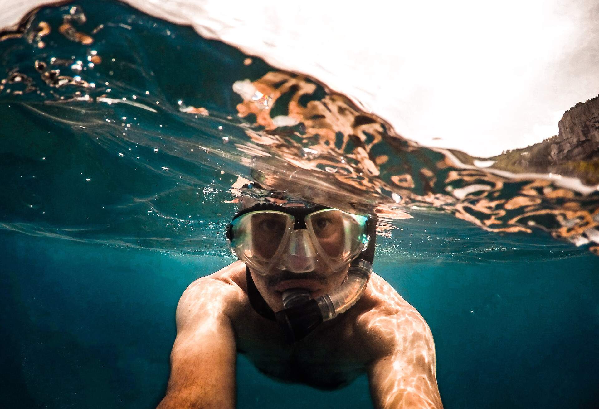 A man with scuba glasses taking a picture underwater