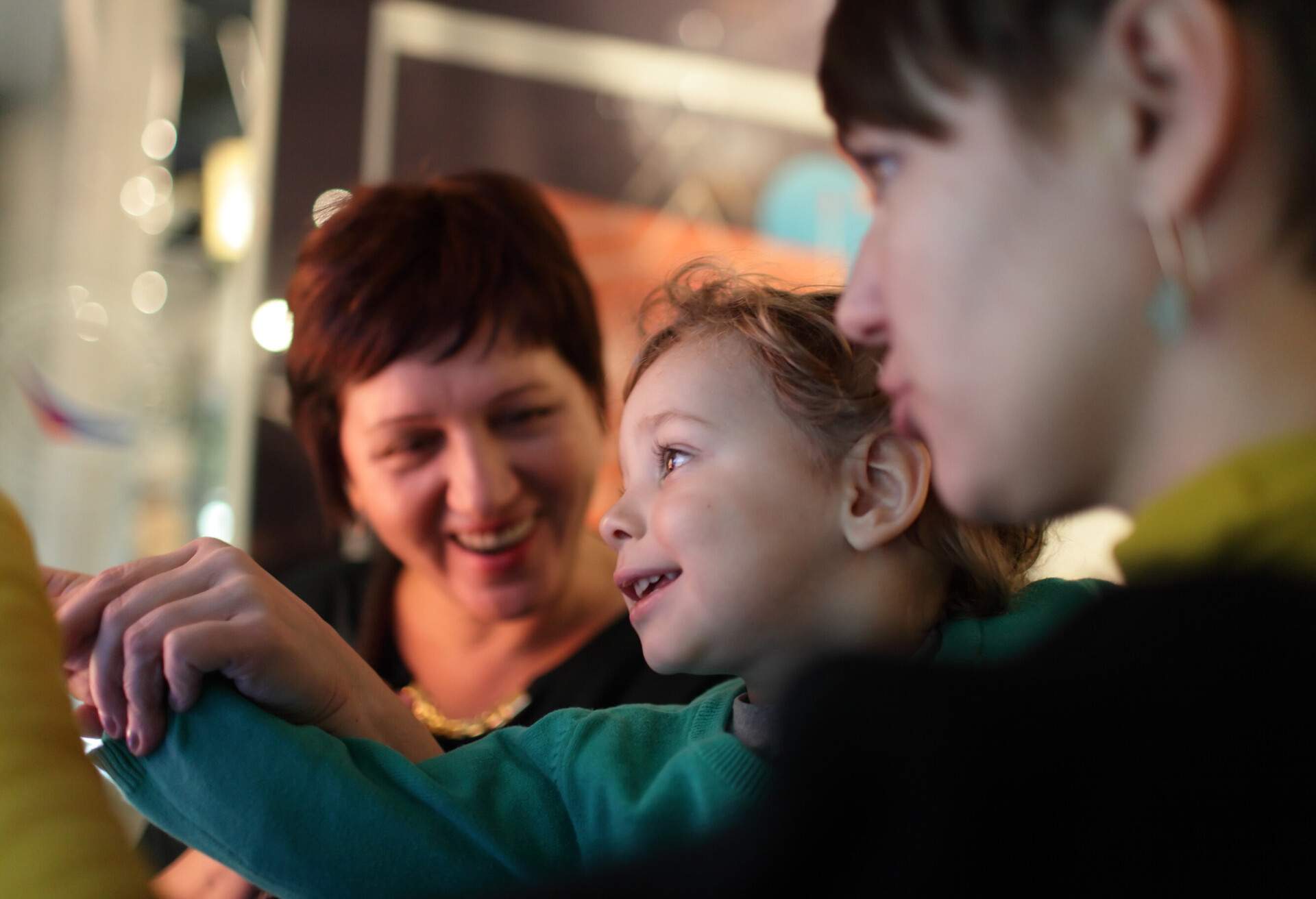 A cheerful person assists a child in pointing at something as the three members of the family look at an exhibit.