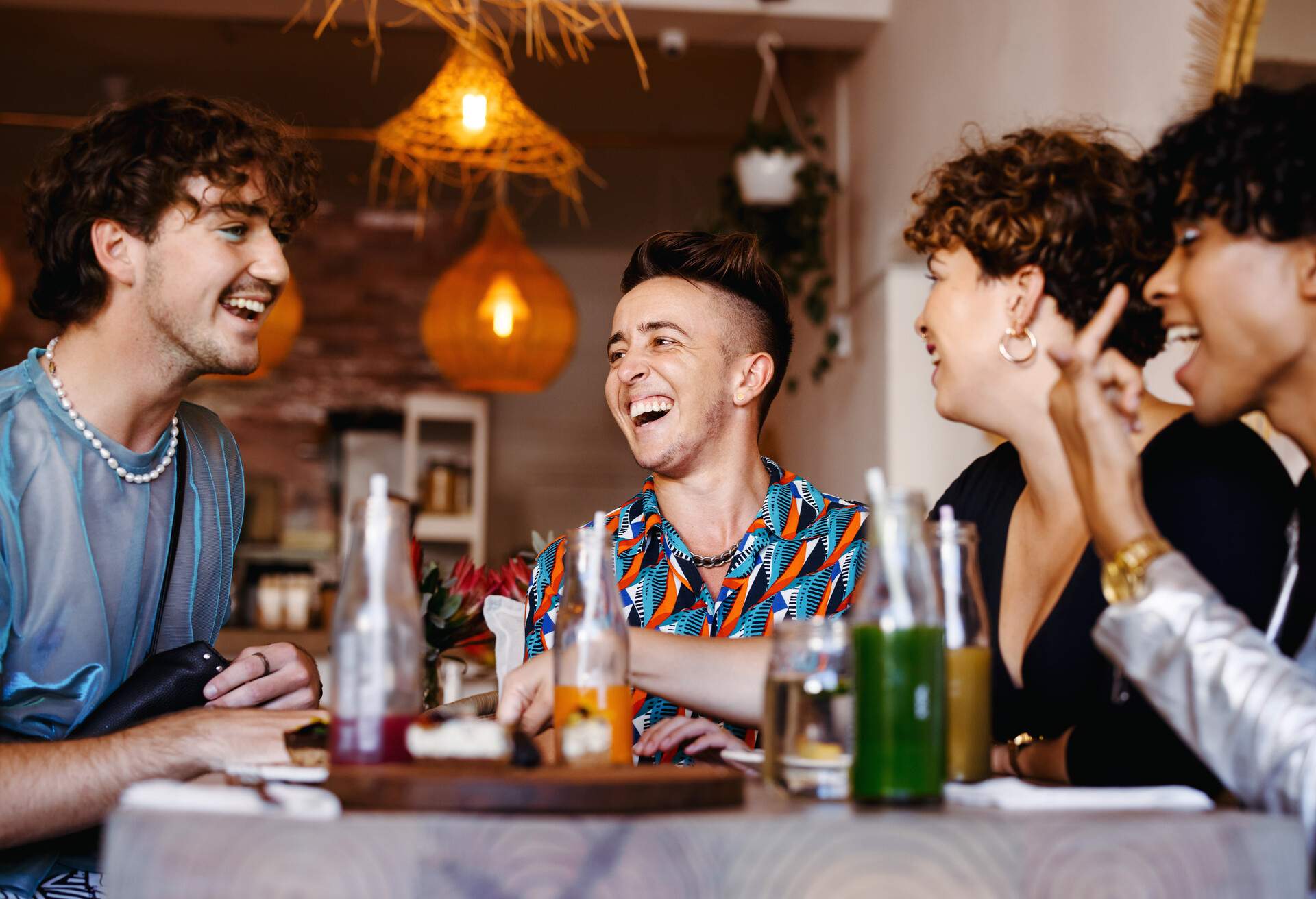 Carefree group of friends laughing together in a restaurant. Four young queer people having fun together during lunch. Friends bonding and spending time together.