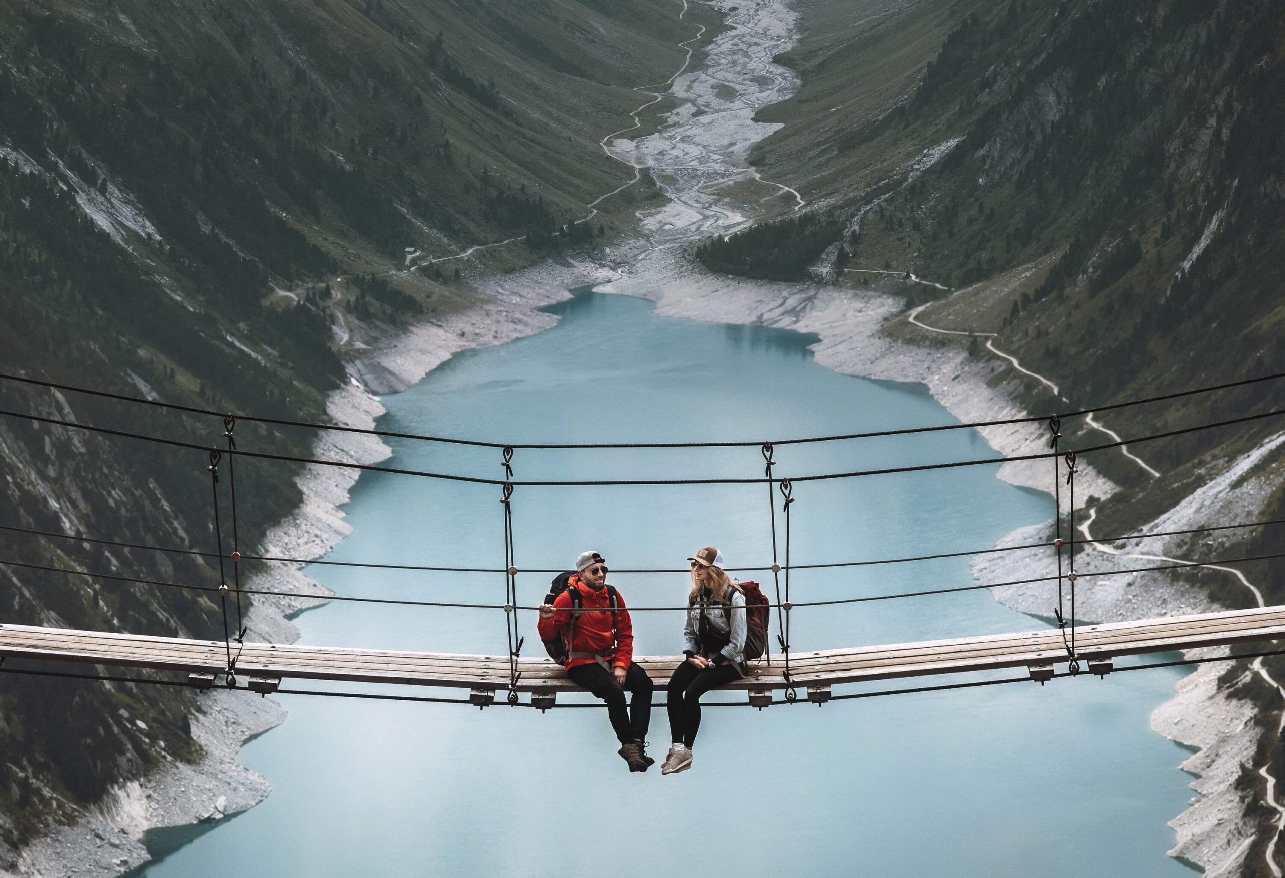 Couple sitting on a suspension bridge in the mountains on top of a lake, Austria