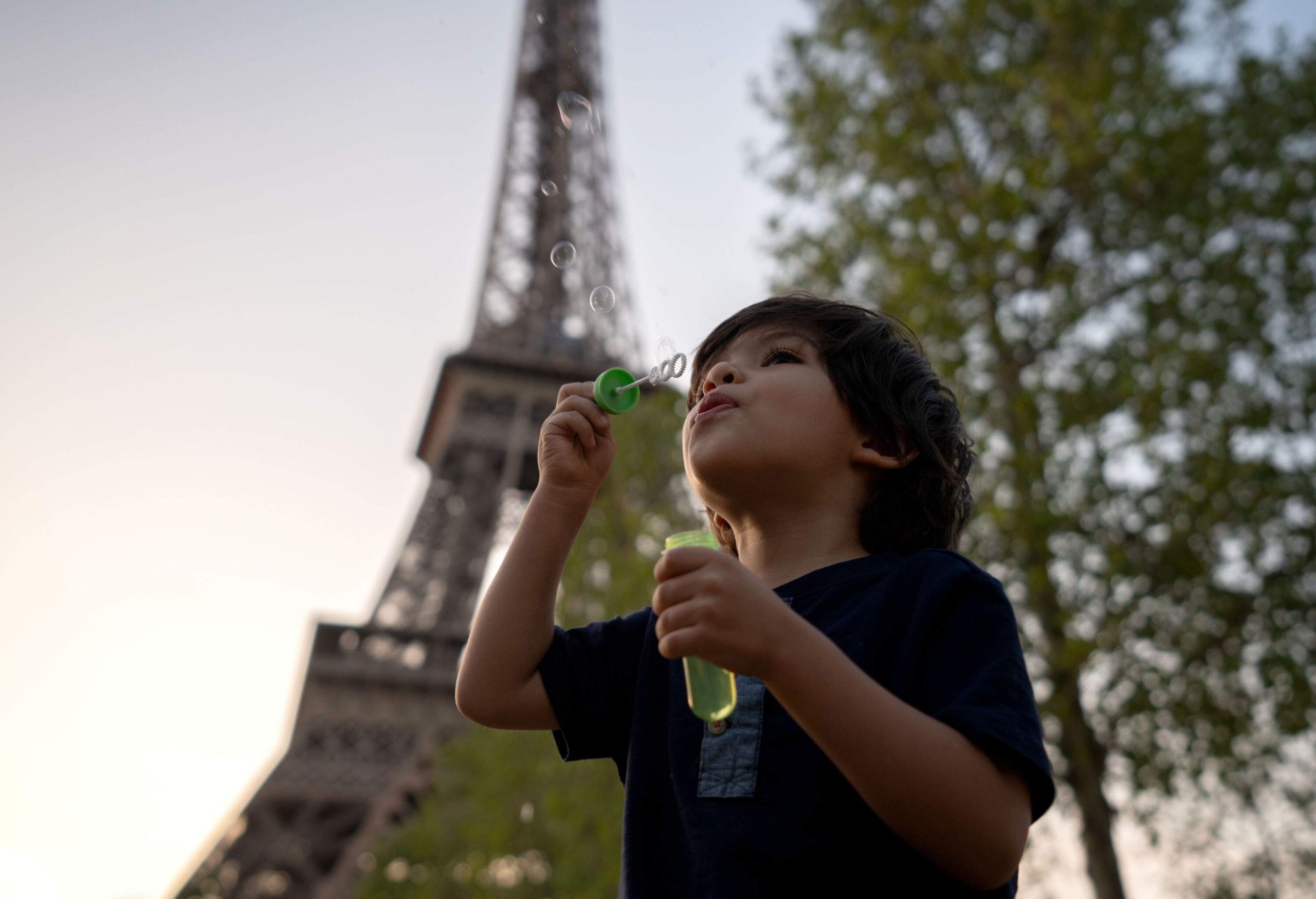 A little boy is blowing bubbles with the Eiffel tower in the background.