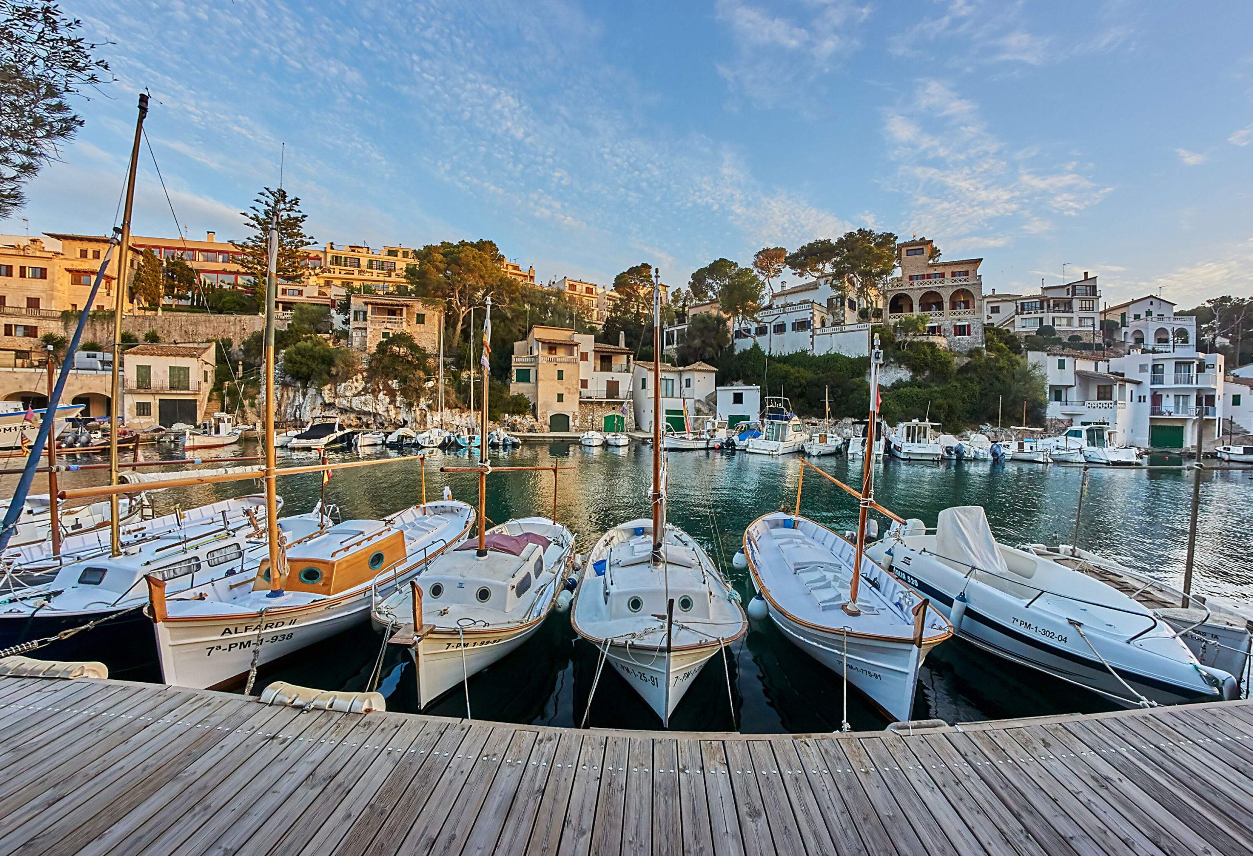 A row of white boats anchored on a wooden pier in a port surrounded by the townscape.