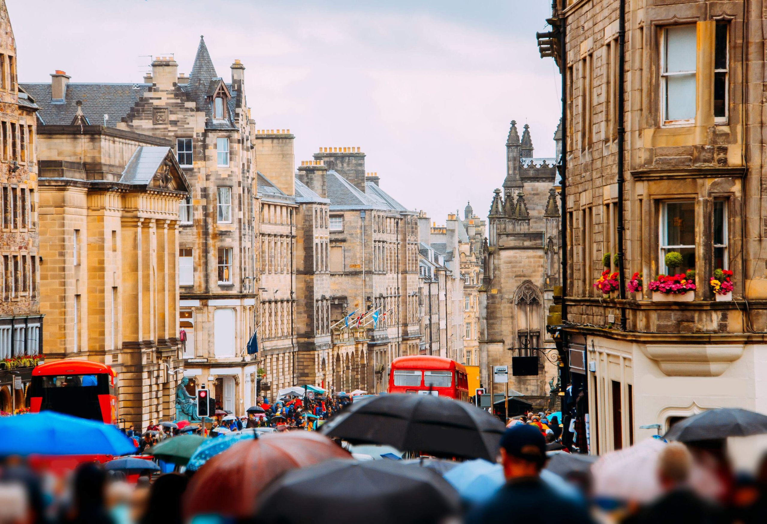 A busy street with people strolling down the sidewalk and red double-decker buses passing along the road.