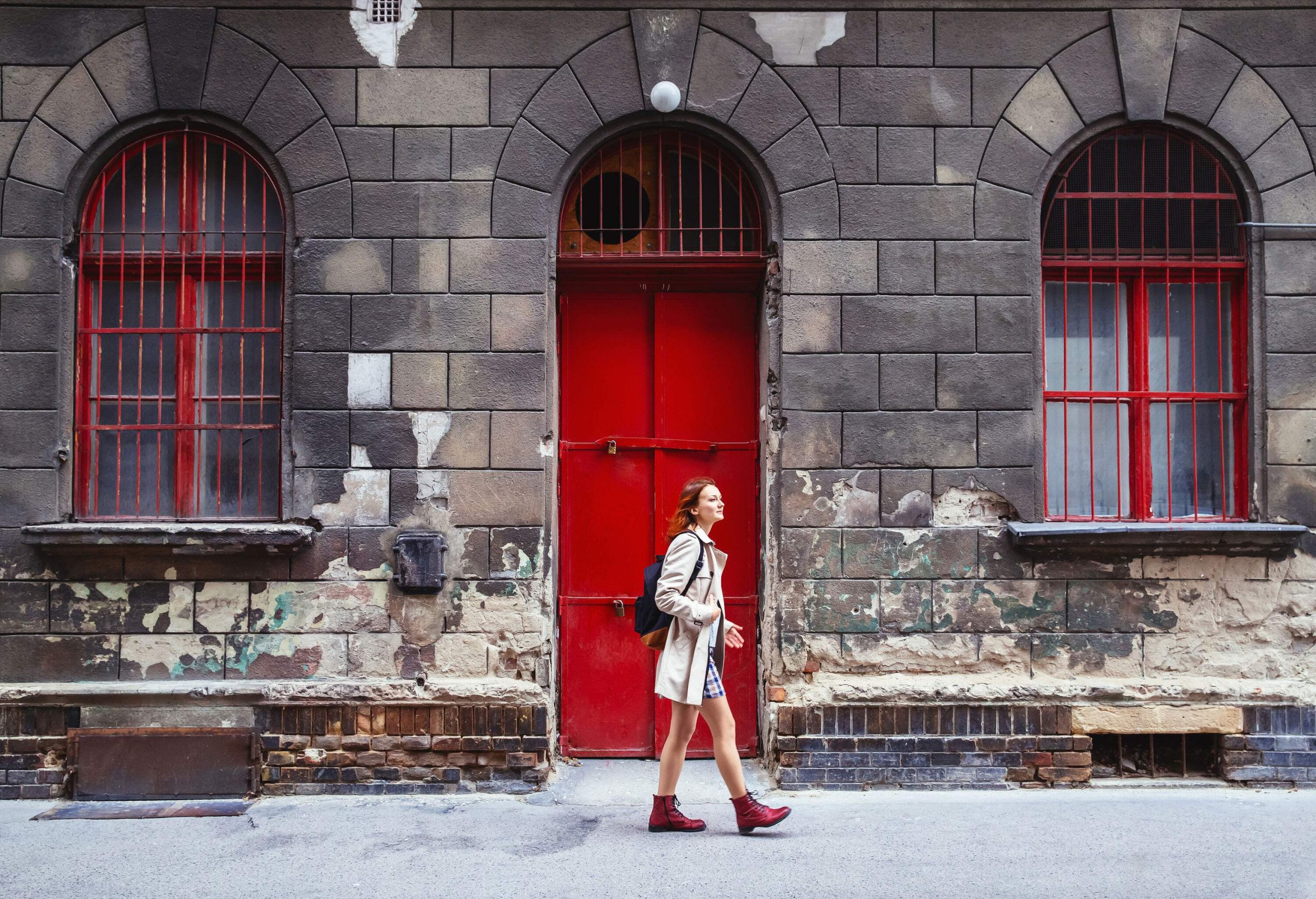 Young lady walking on a sidewalk next to a building with a red door.