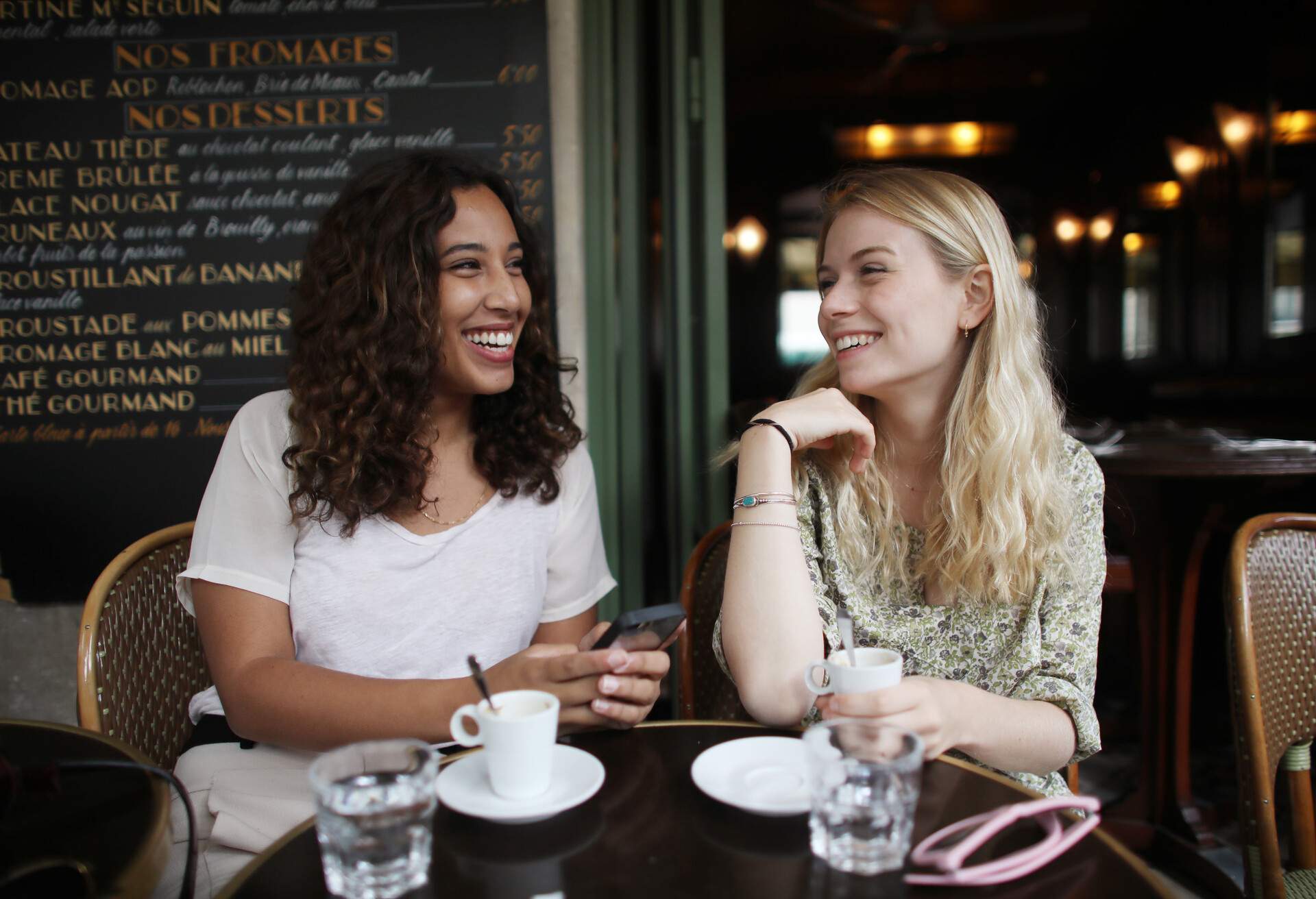 Two female friends smiling at each other in a café in Paris, France