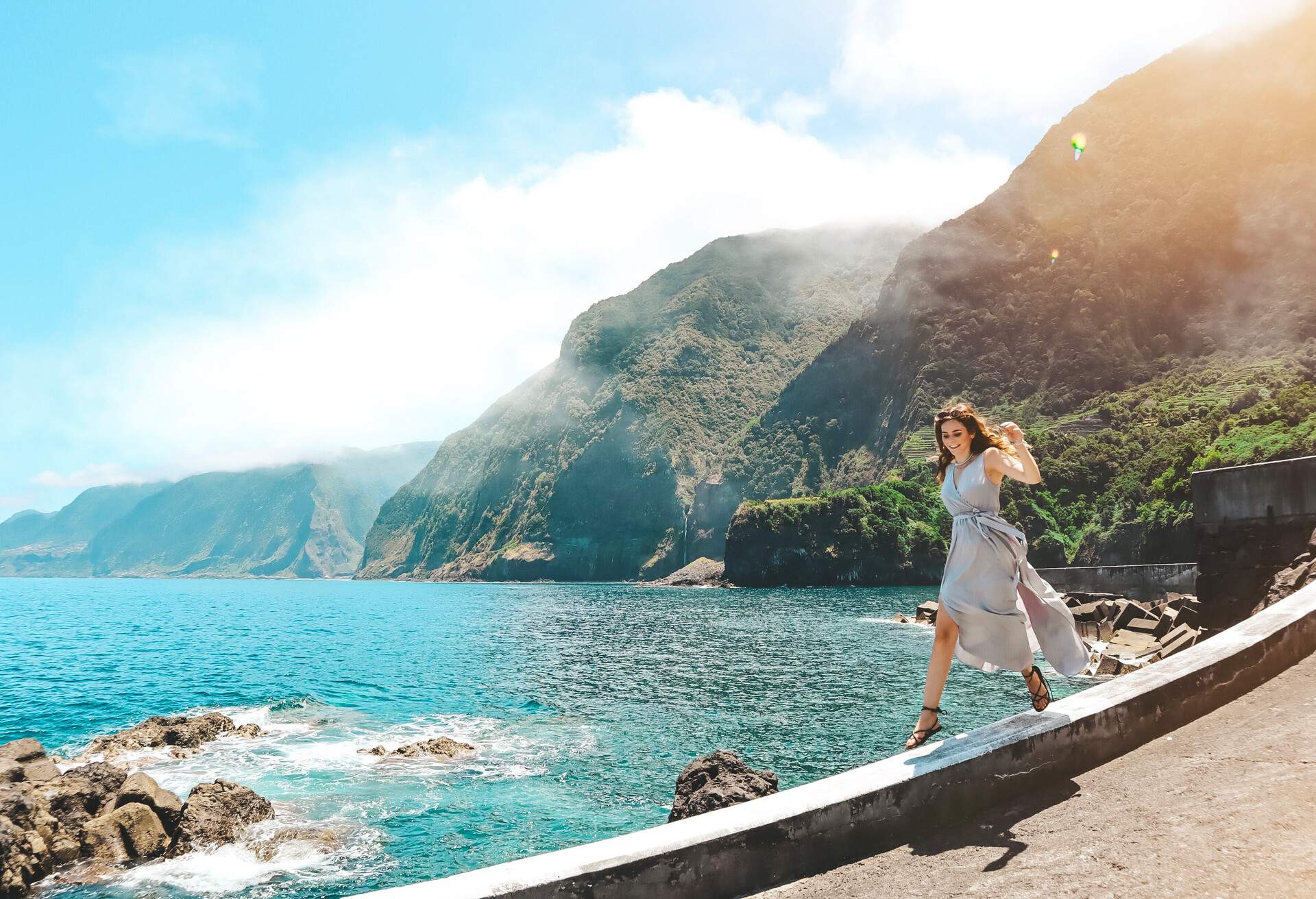 Womanon ledge by the sea with mountains in the background Portugal, Madeira Island.