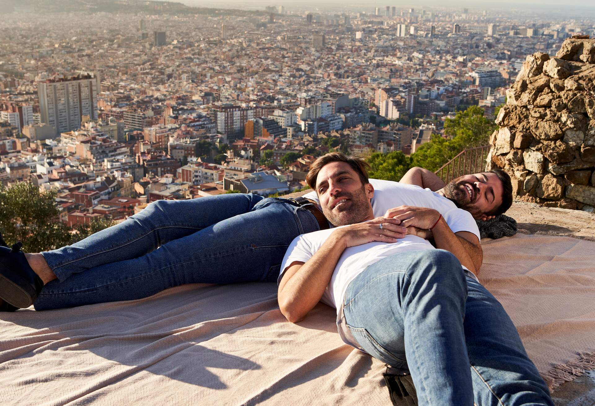 LGBTQ gay couple lying on an observation point with a view of Barcelona cityscape, Spain