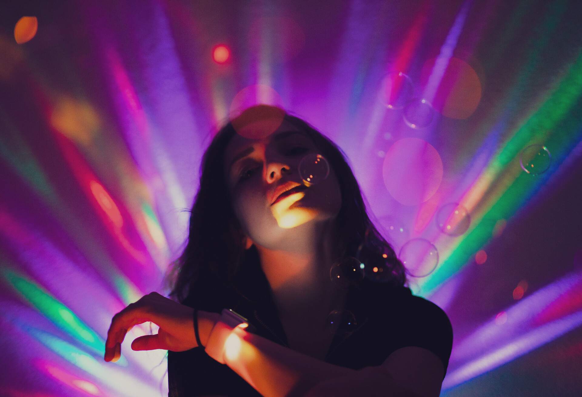 A woman chilling in the dark surrounded by floating bubbles and colourful light streaks.