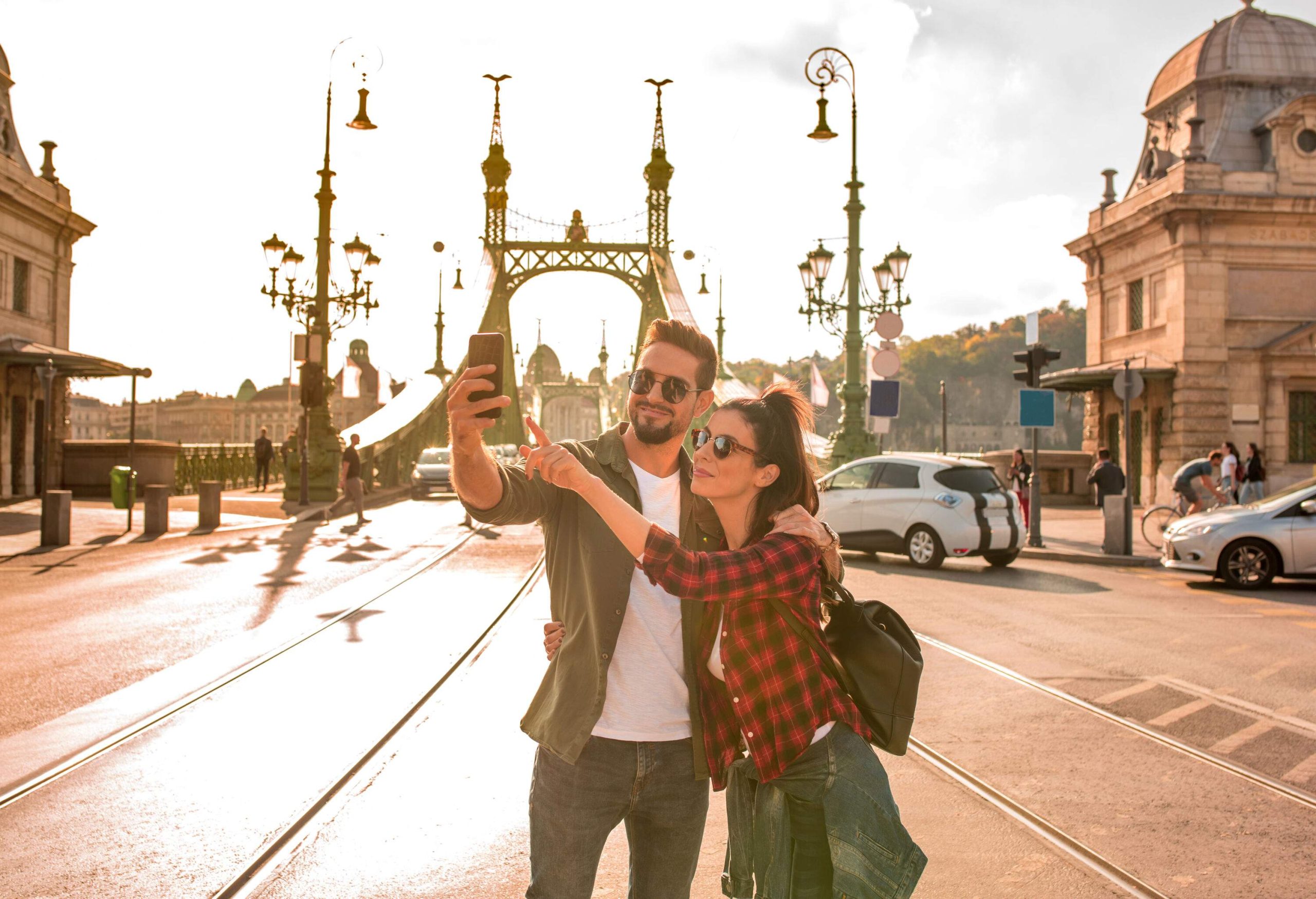 A happy couple takes a selfie with a famous and busy Liberty bridge in Budapest, Hungary.