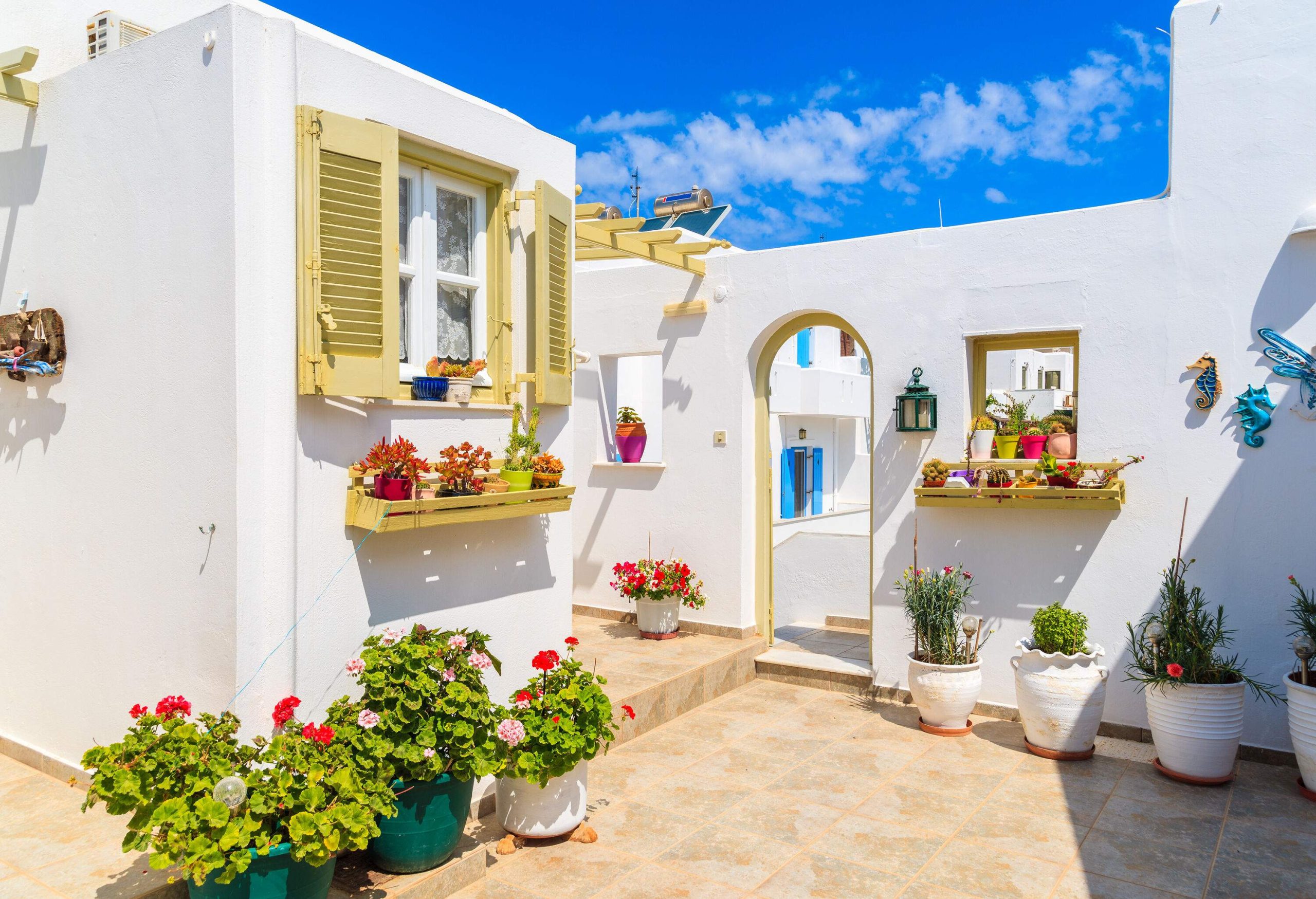 A charming white villa with a patio adorned with potted plants and coastal wall décor.
