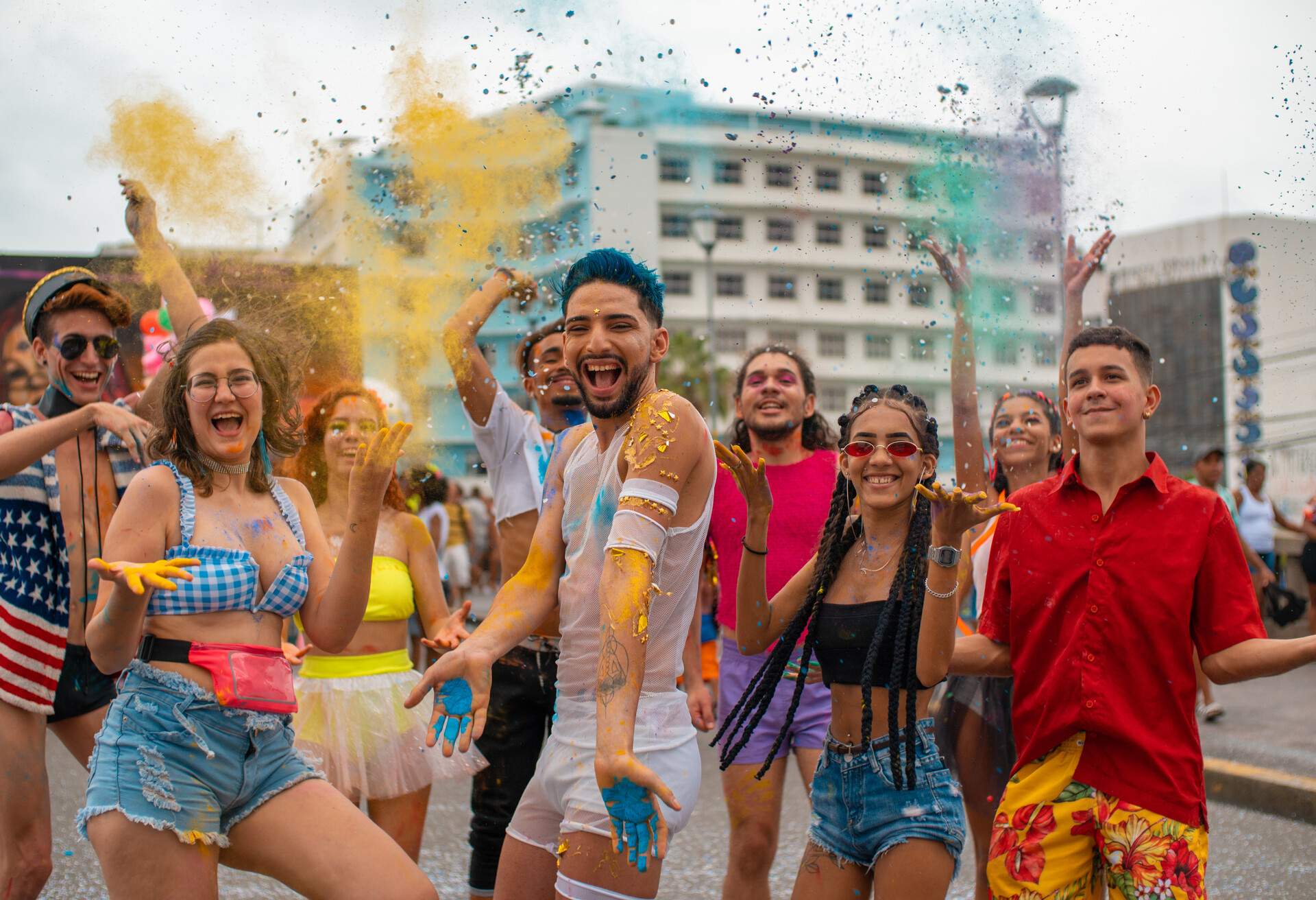 A group of young individuals in their swimwear throwing colourful confetti and powders during a festival.
