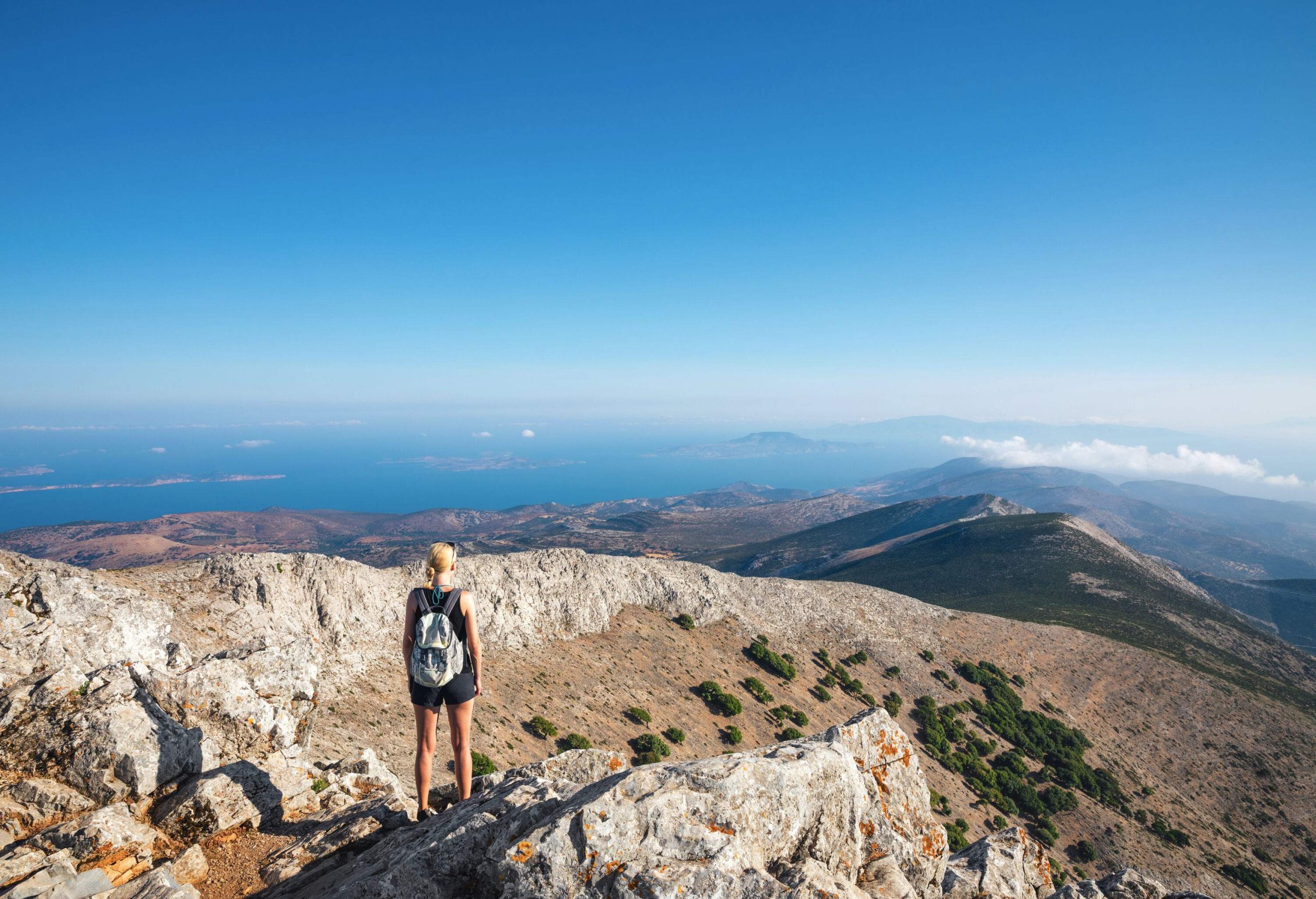 Woman standing at a rocky summit overlooking the mountains on the horizon.
