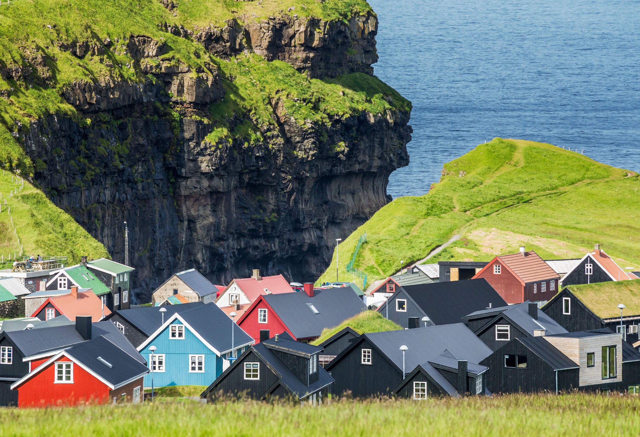 A green cliff topped with colourful houses overlooking the sea.