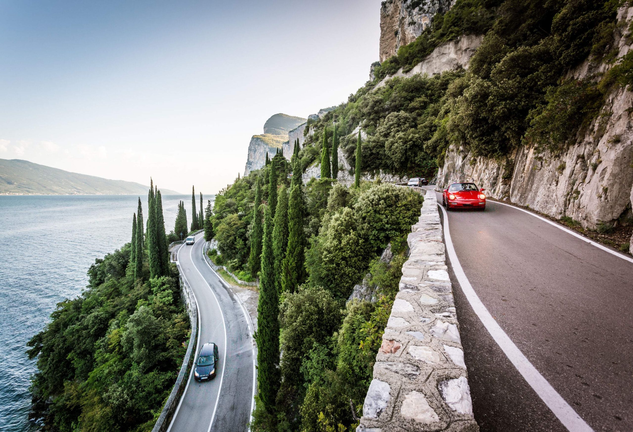 A road on a rocky mountain lined with green trees overlooking the sea below.