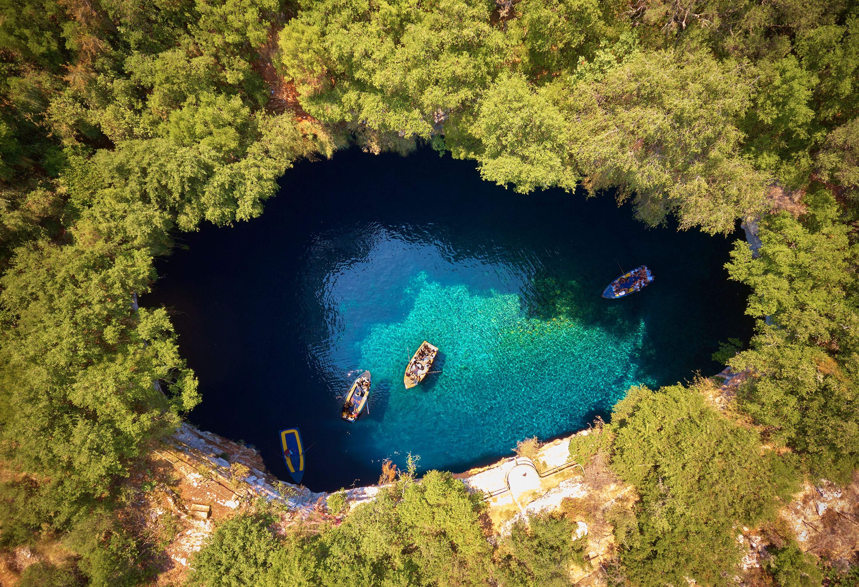 Aerial view of boats inside the cave surrounded by lush forest on a cliff.