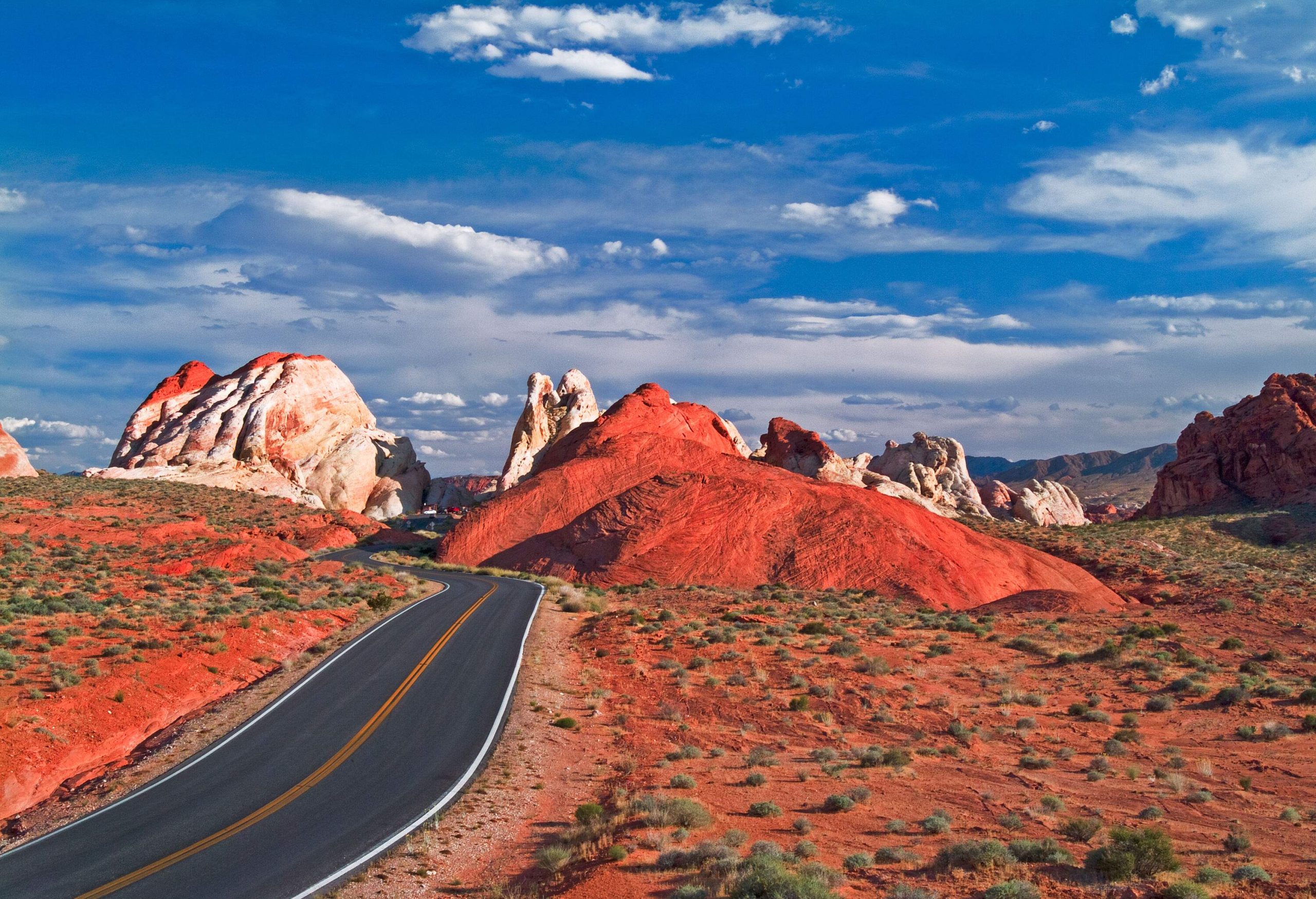 An empty asphalt road meandering on a stunning red rugged valley under a dramatic sky.