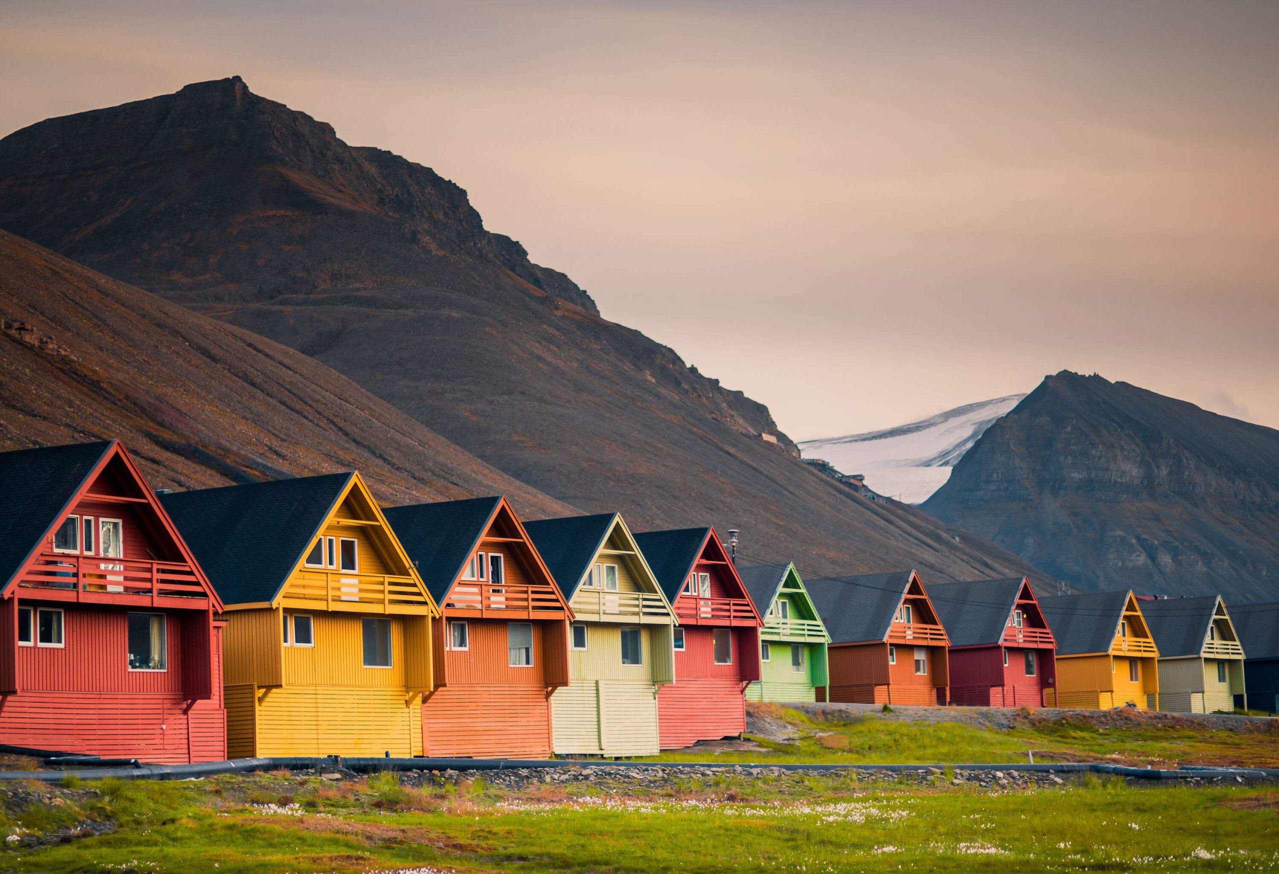 A row of wooden cabins with colourful façades at the foot of the mountains.