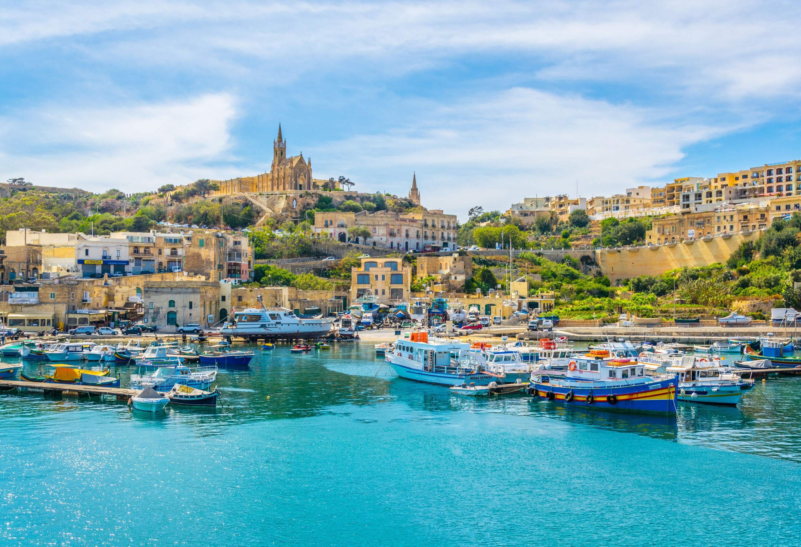 A bustling port town with boats moored in the harbour and historic structures dotting the coastline.