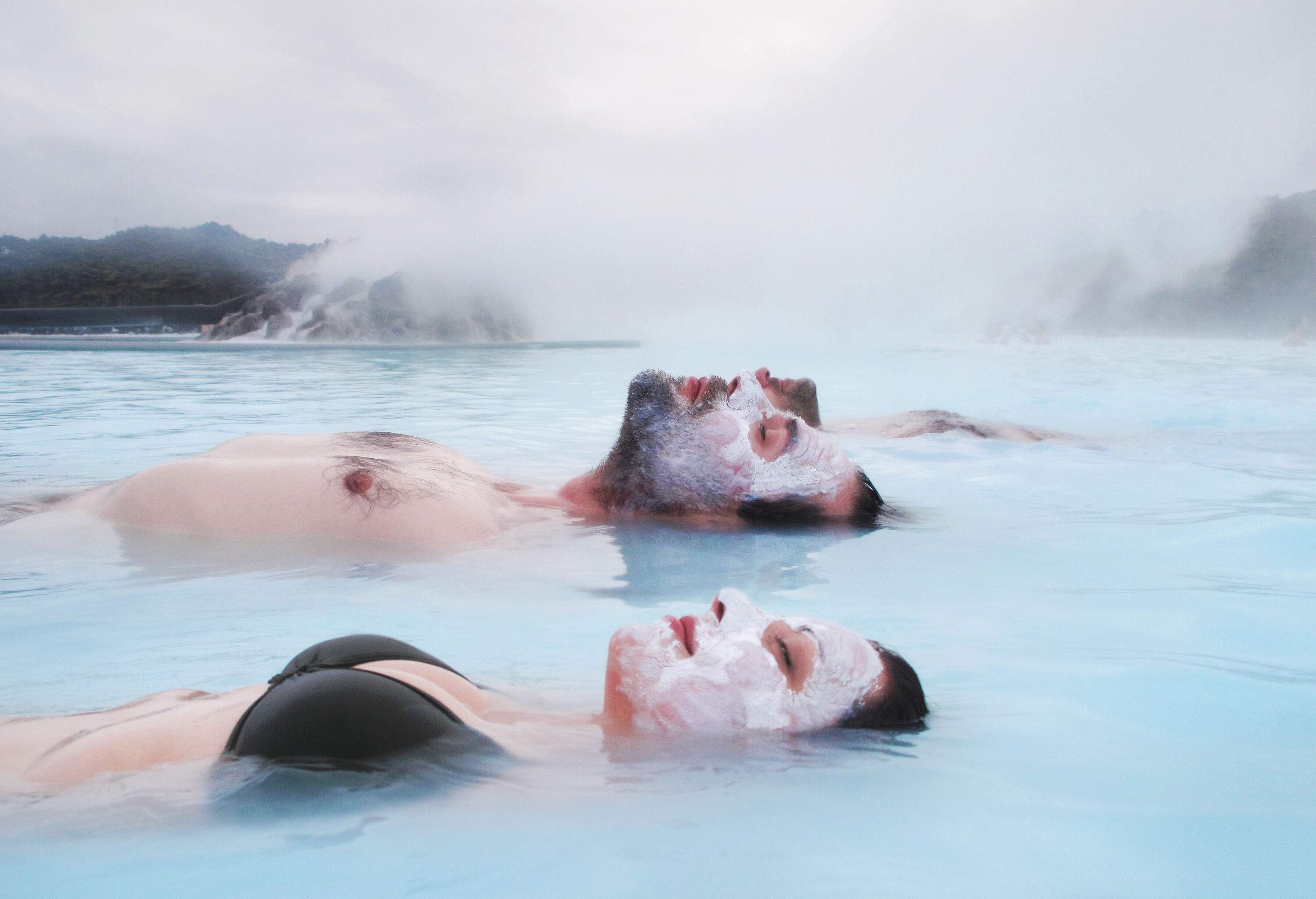 A couple with white masks on their face floating in the steamy thermal pool.