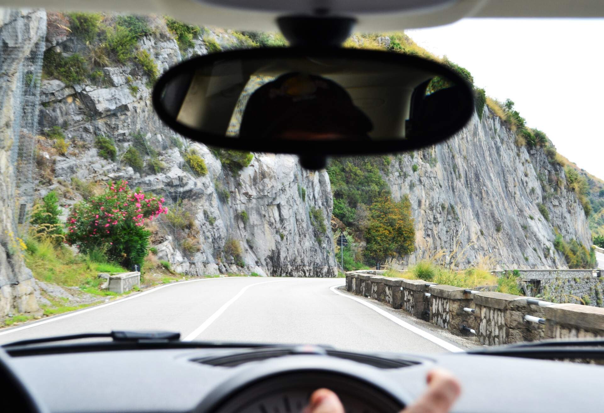 A car's front view of an empty road along a steep cliff.