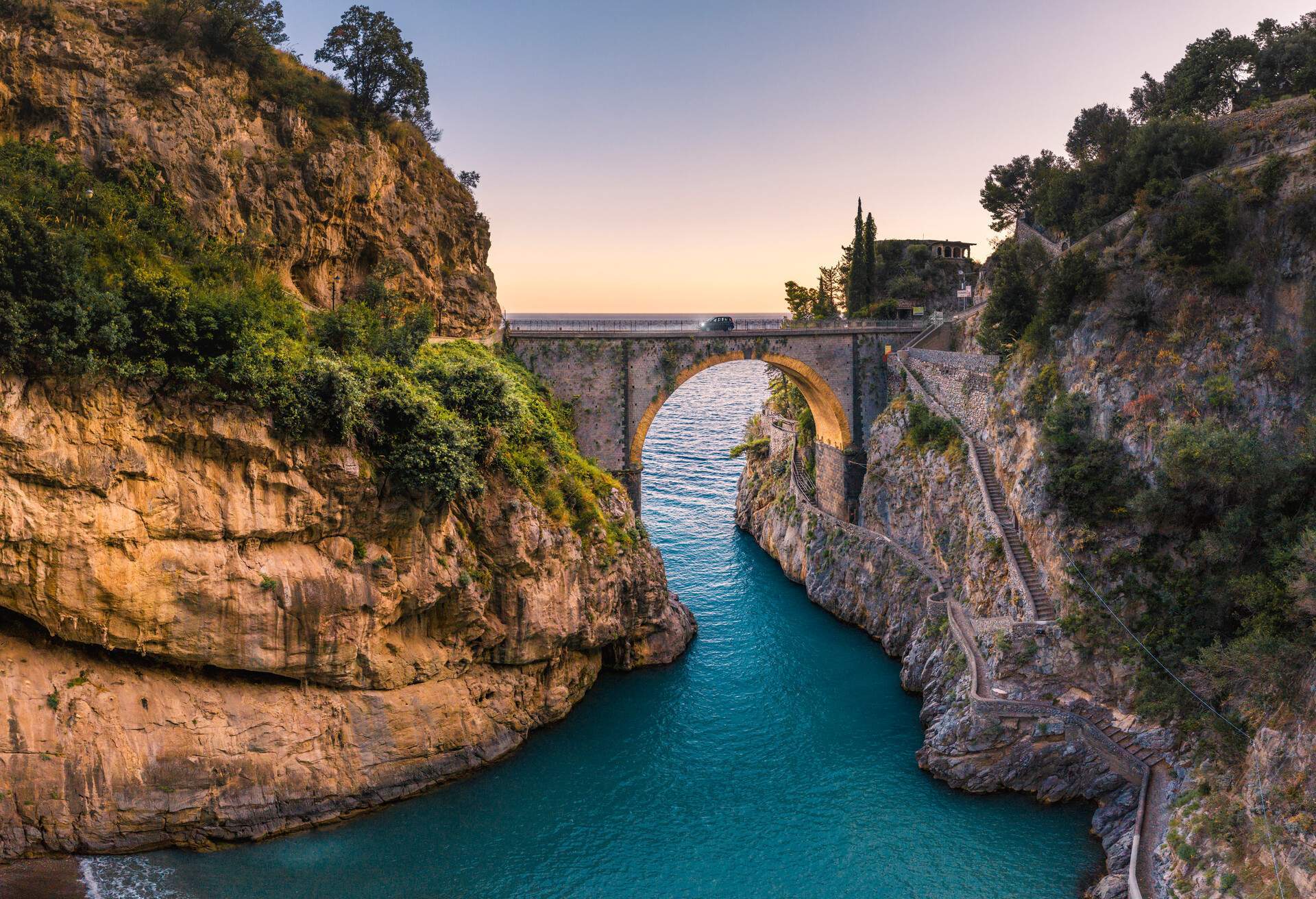 A car driving through a single-arch bridge across the picturesque Furore Fjord.