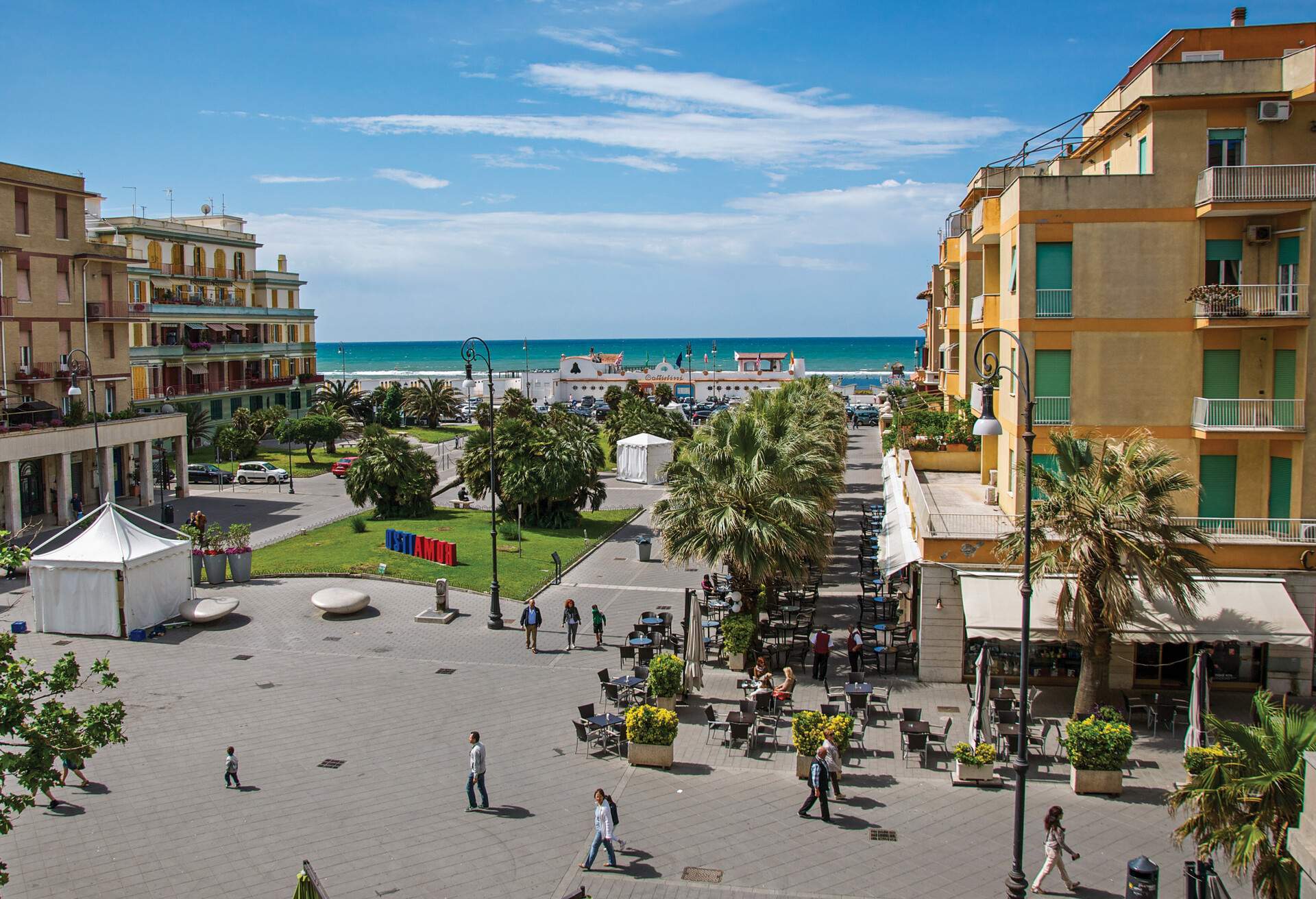 Aerial view of a coastal city with a plaza surrounded by buildings overlooking the tranquil blue sea.