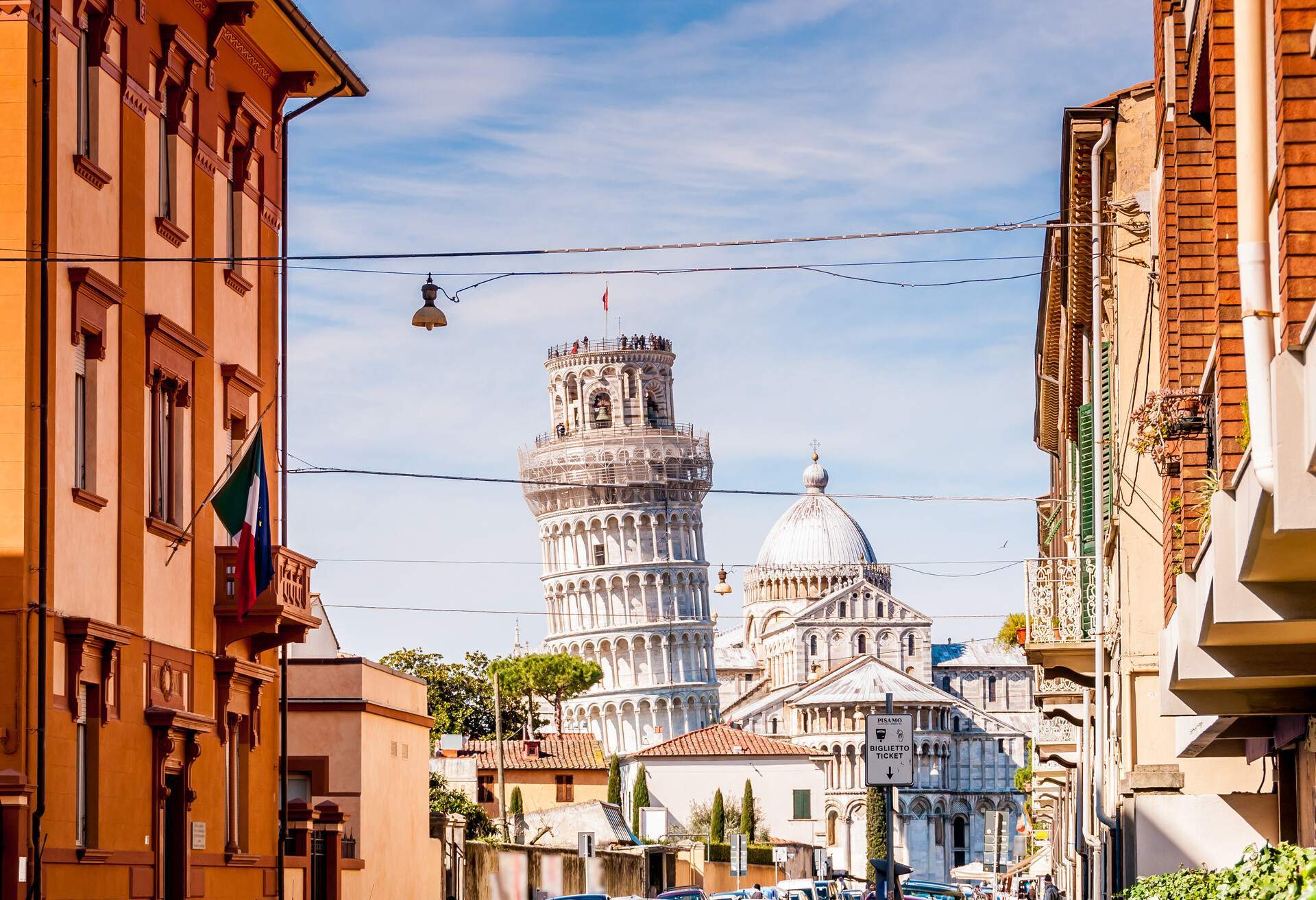 A charming street in Pisa leads to the iconic Campanile and cathedral in the distance.
