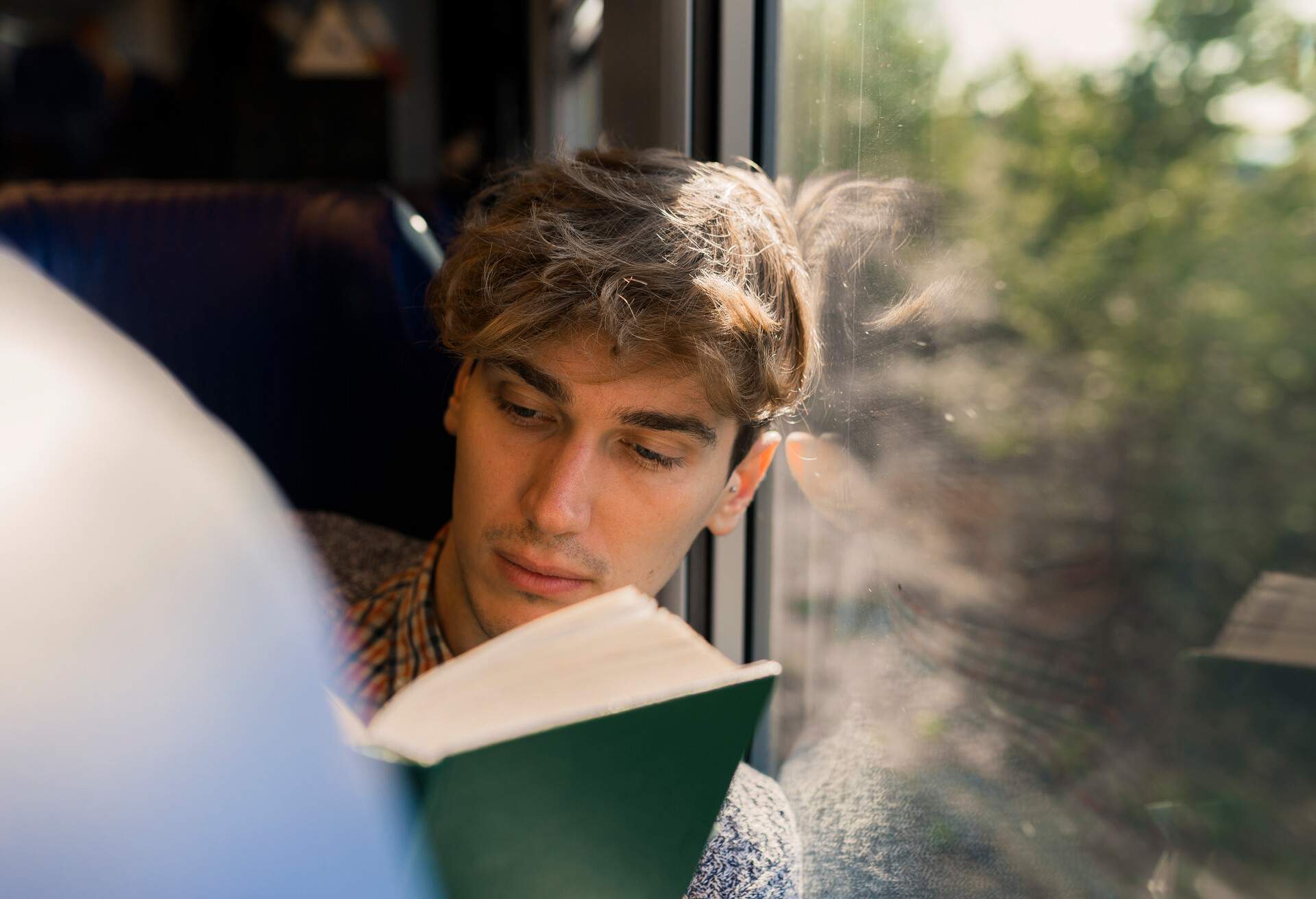 A young man reading a book while travelling on a train.