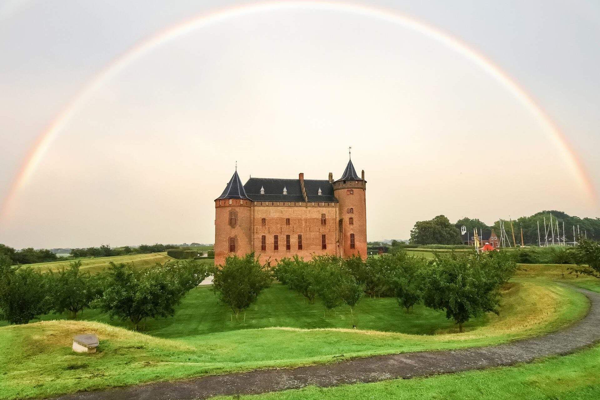 An enchanting rainbow forms an arch above the castle in a grassland.