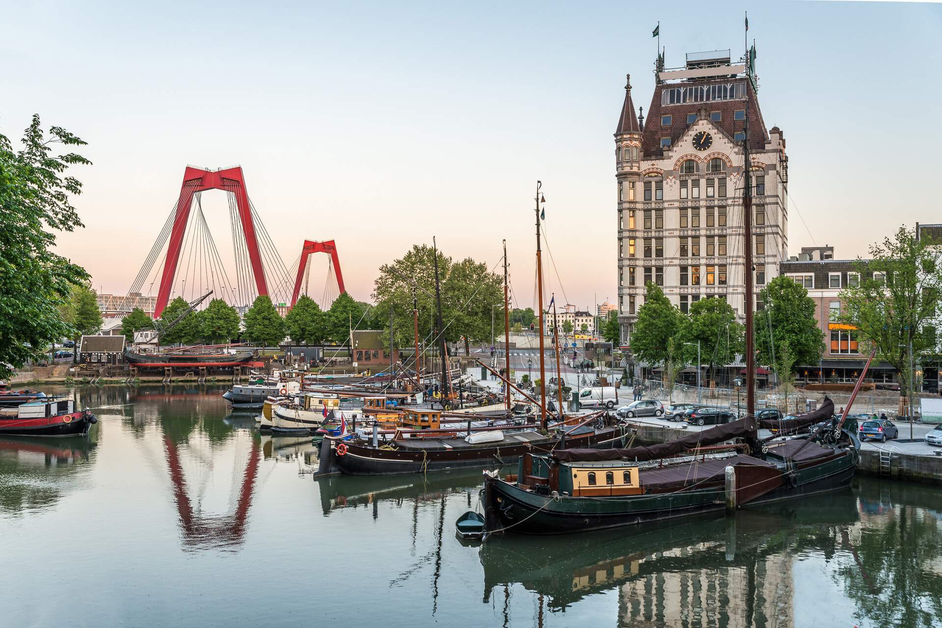 Old ships moored in a historic harbour with a view of an art nouveau building against the scenic twilight sky.