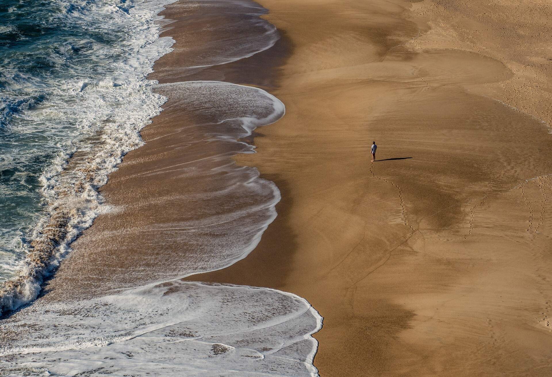 Man standing on empty beach in Nazaré, Portugal