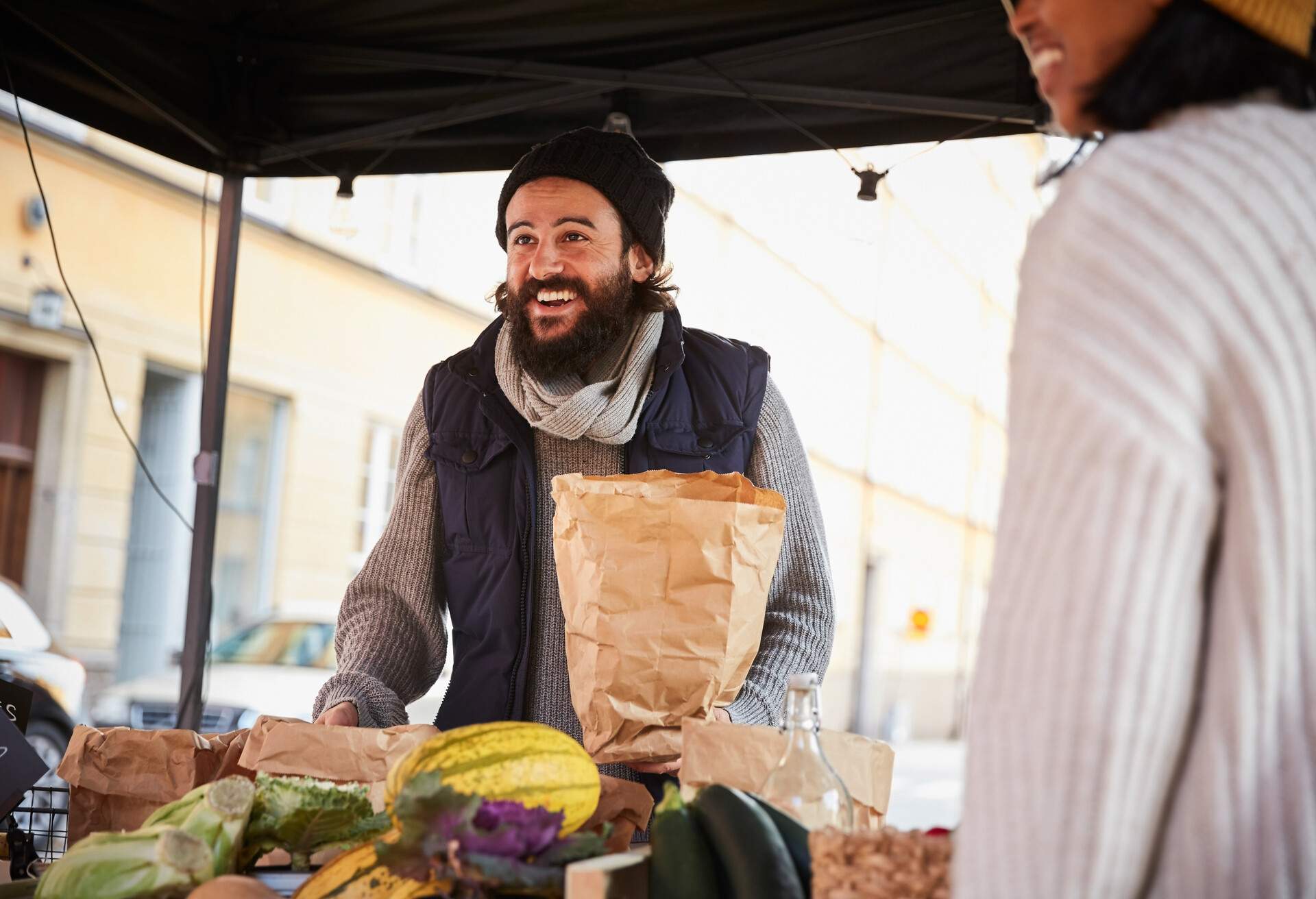 Smiling man buying vegetables from female vendor at market stall, Stockholm, Sweden.