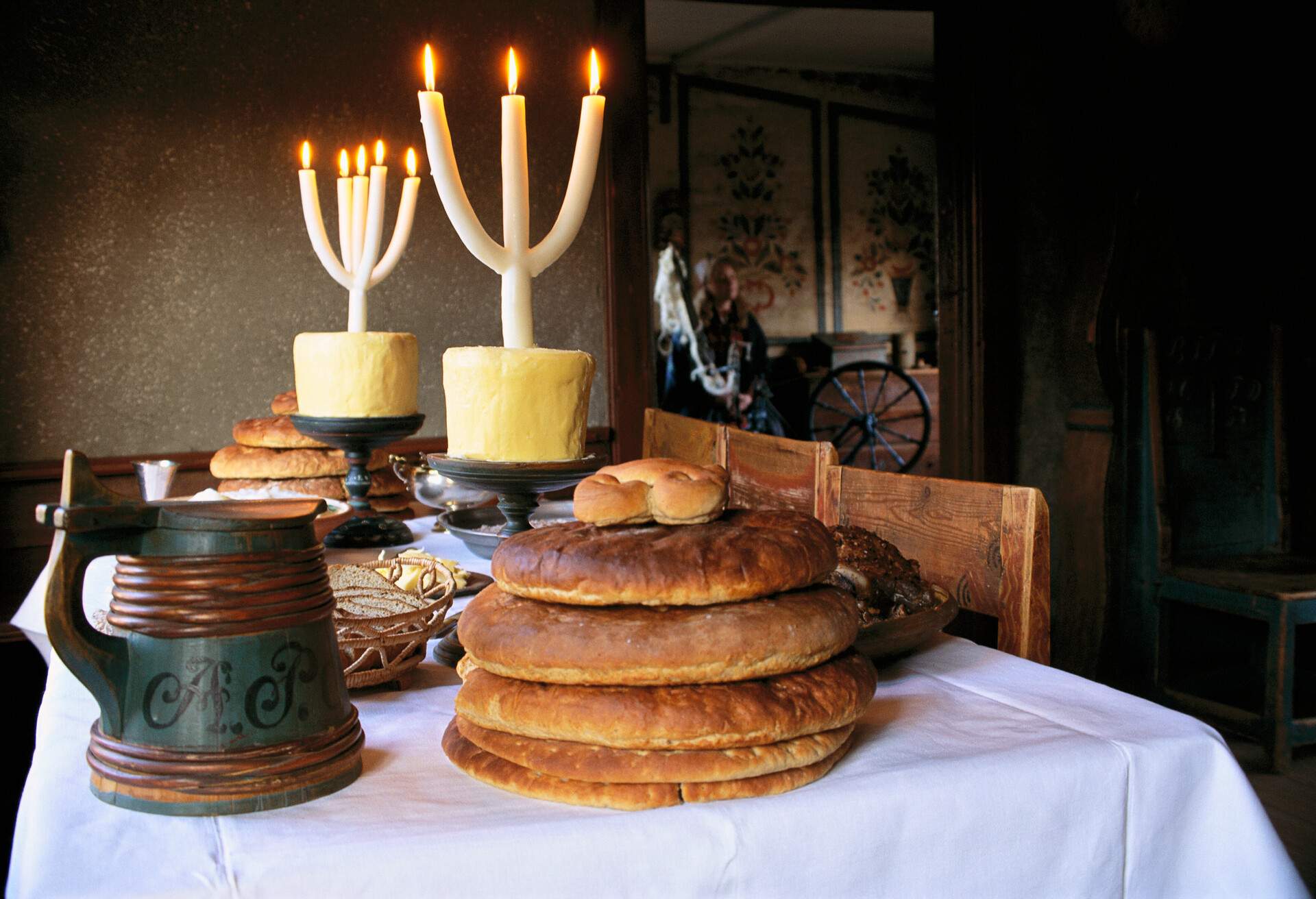 A dinner table with a white tablecloth, plates of bread and cheese, and fork-shaped candles perched on candlesticks.