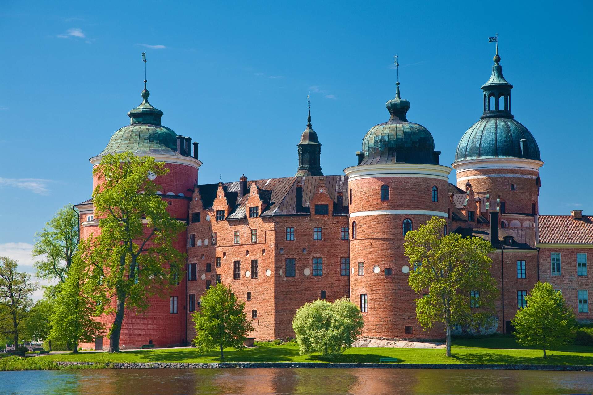 Gripsholm Castle is a renaissance castle with orange walls, round towers, and dome roofs with sharp pinnacles.