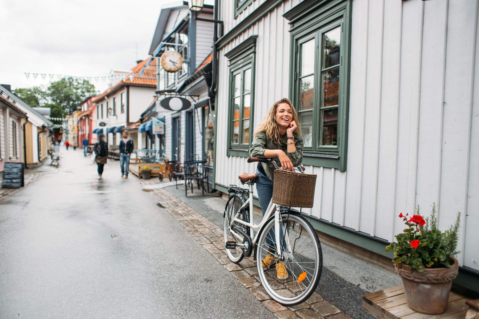 A woman standing with her bike on a rainy day in a street with wooden houses