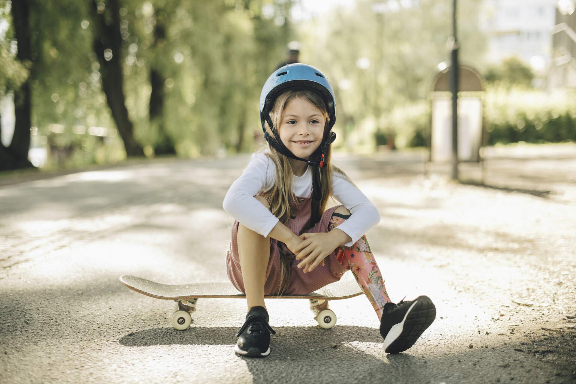 A young girl with a prosthetic leg and a blue helmet sitting on a skateboard
