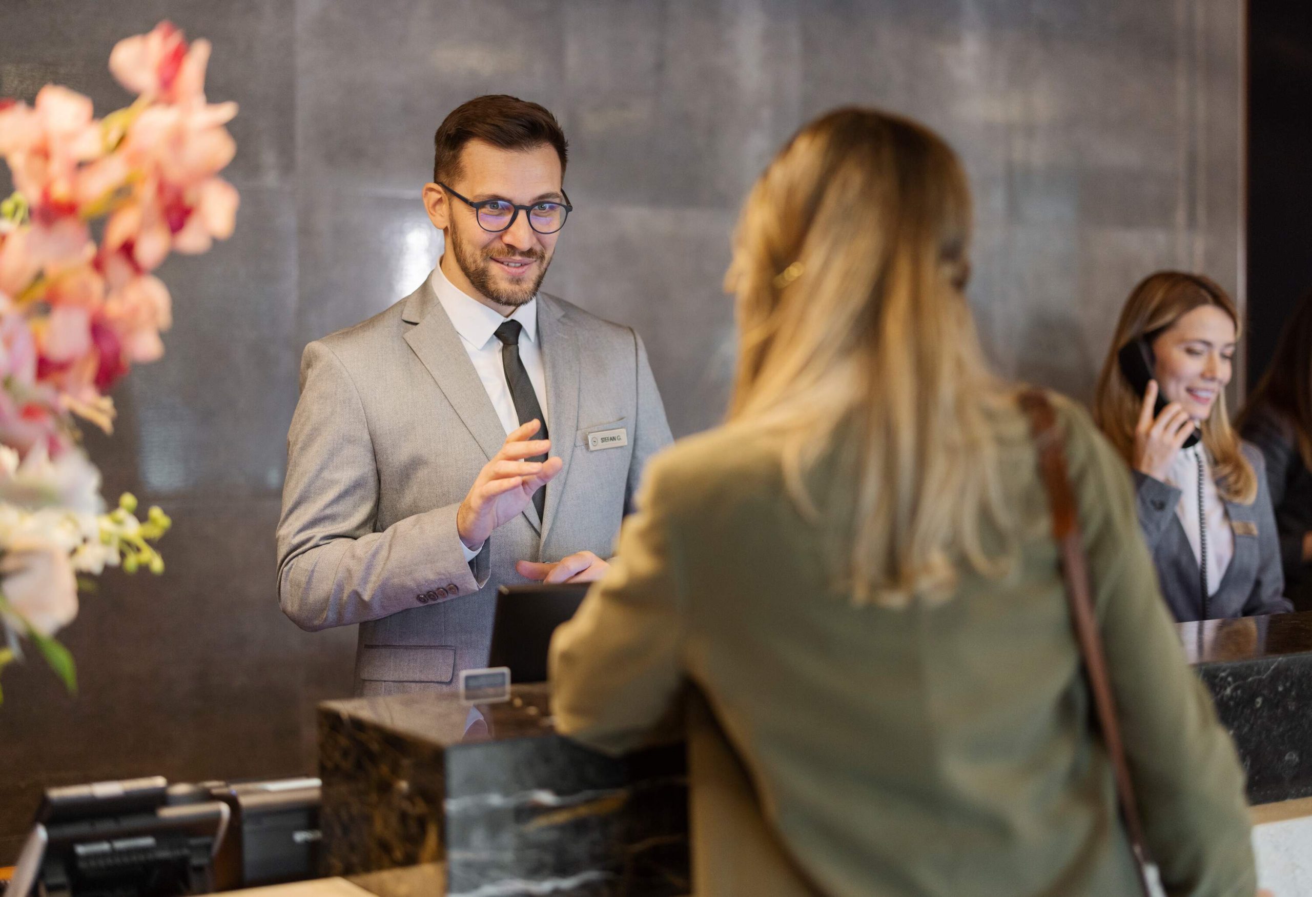 theme_travel_vacation_hotel_front_desk_receptionist_male_guest_female_people_gettyimages-1448506102