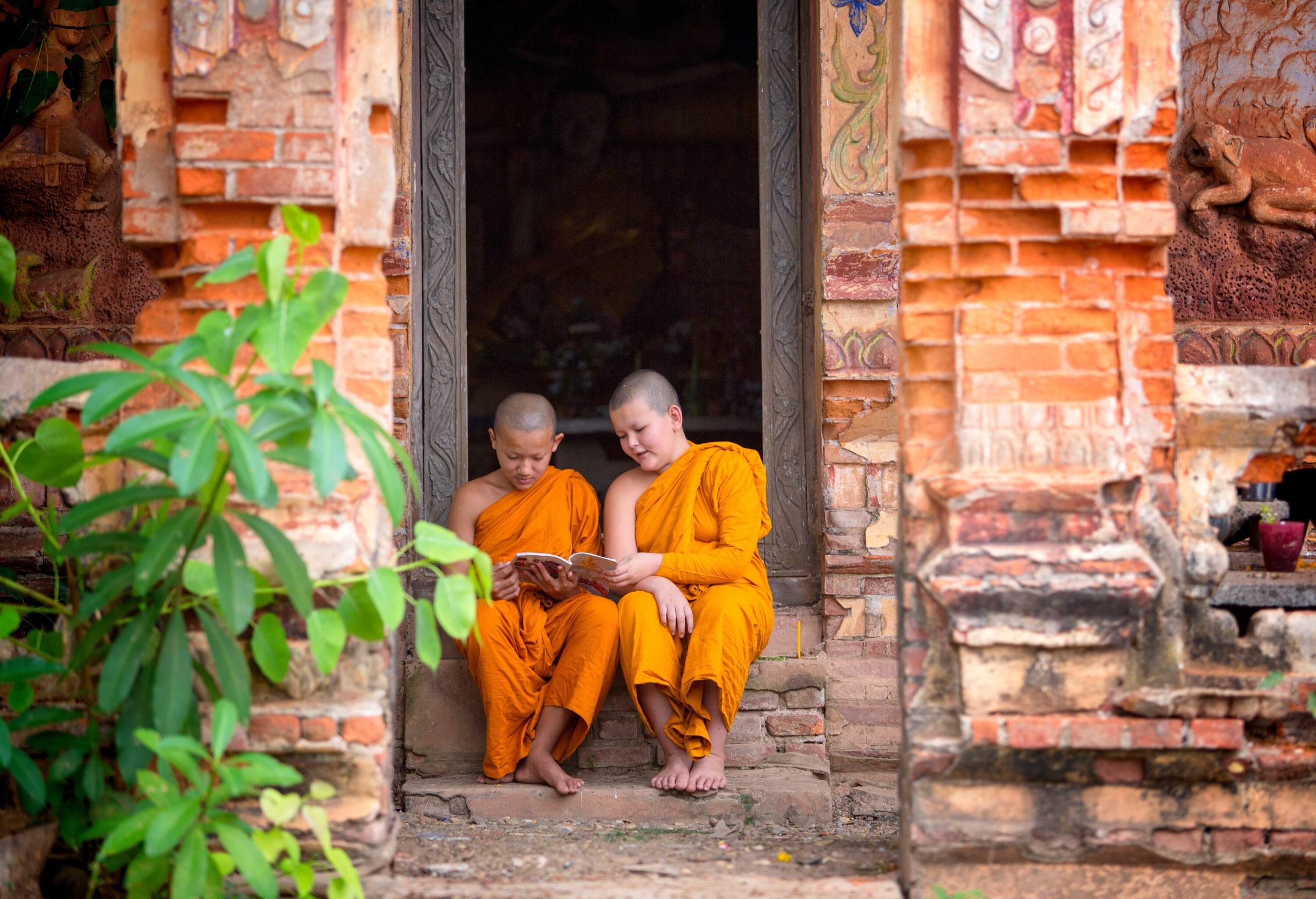 Two novice monks reading a booklet while sitting on a staircase in a temple.