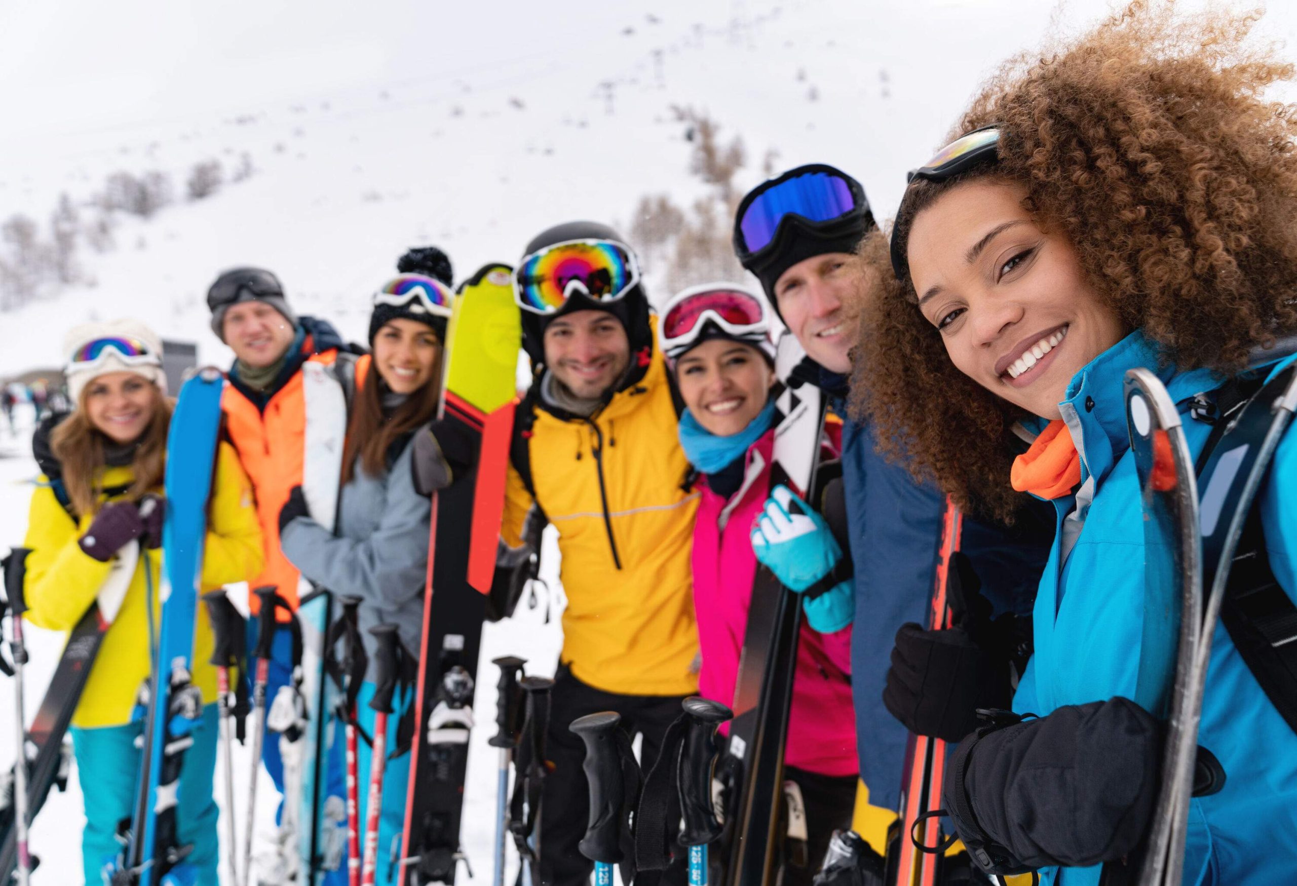 A smiling group of friends in colourful winter clothes lined up together holding their snowboards.