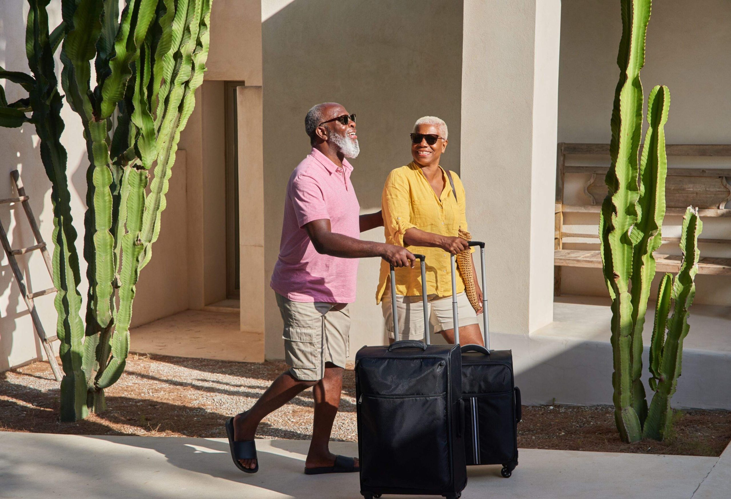 A mature couple walk luggage up the entrance of a luxury villa (long lens).