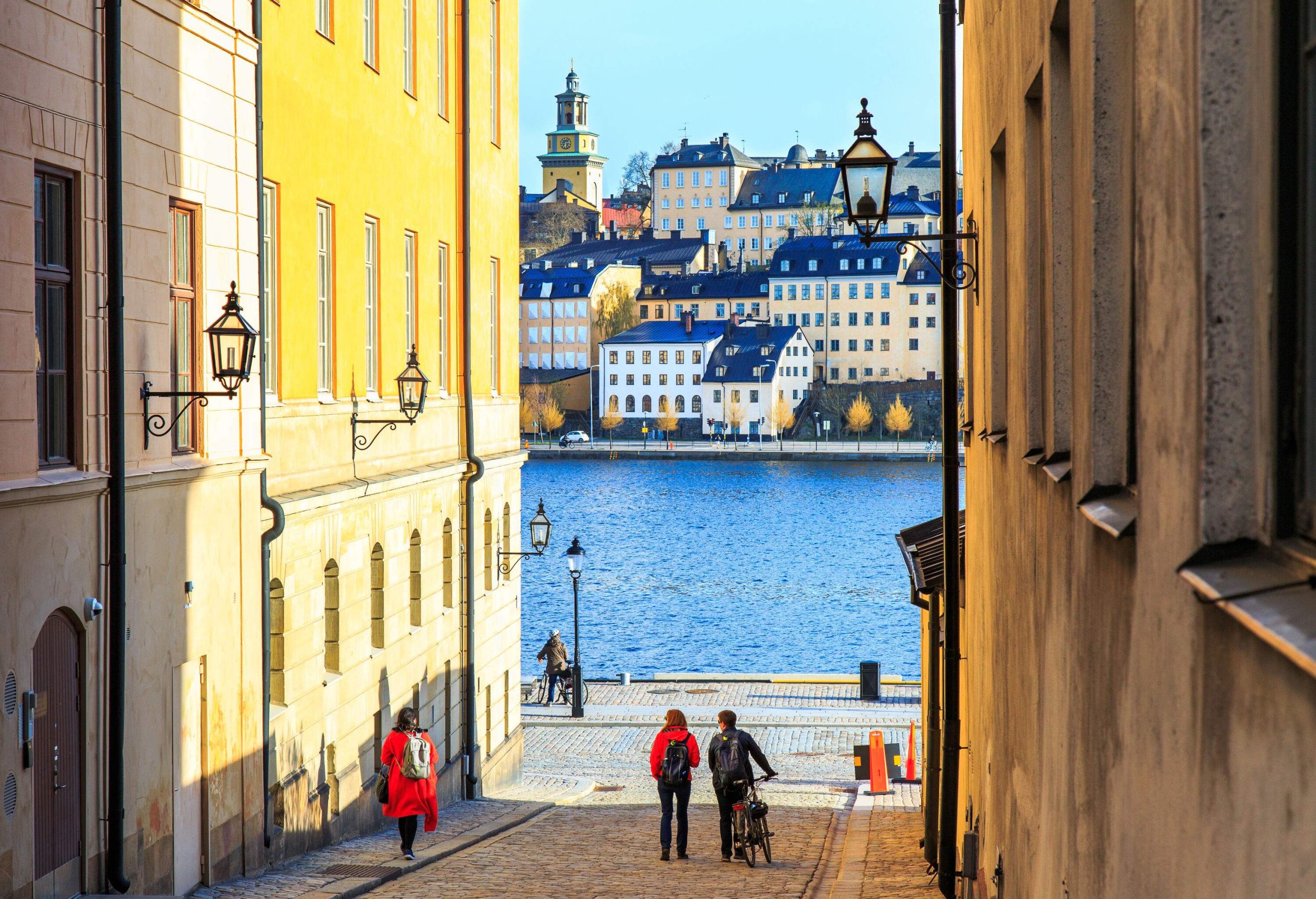 People on a cobbled street with a view of classic and elegant buildings across the waters.