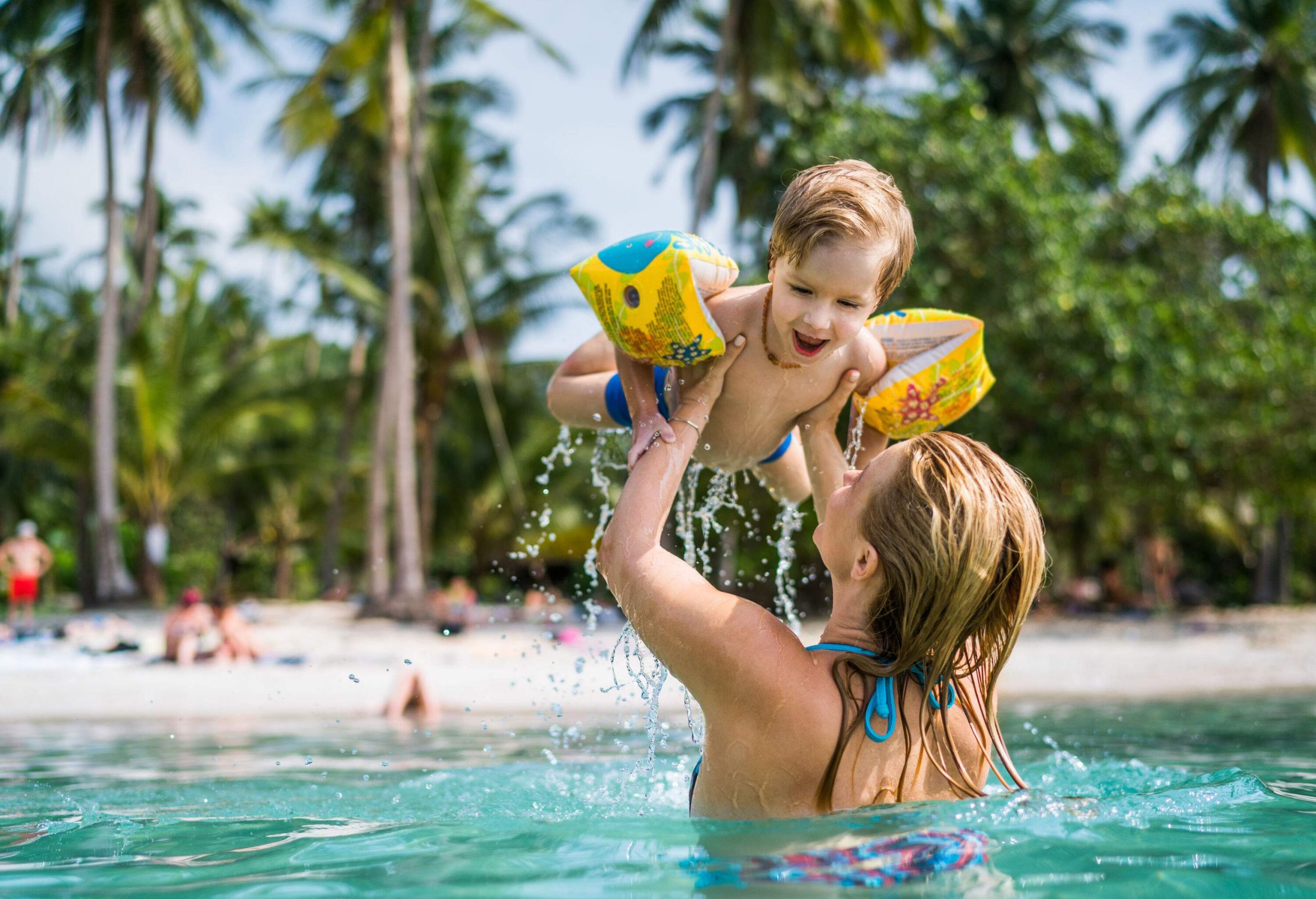 A woman lifting a little boy in the air as they play in the sea.