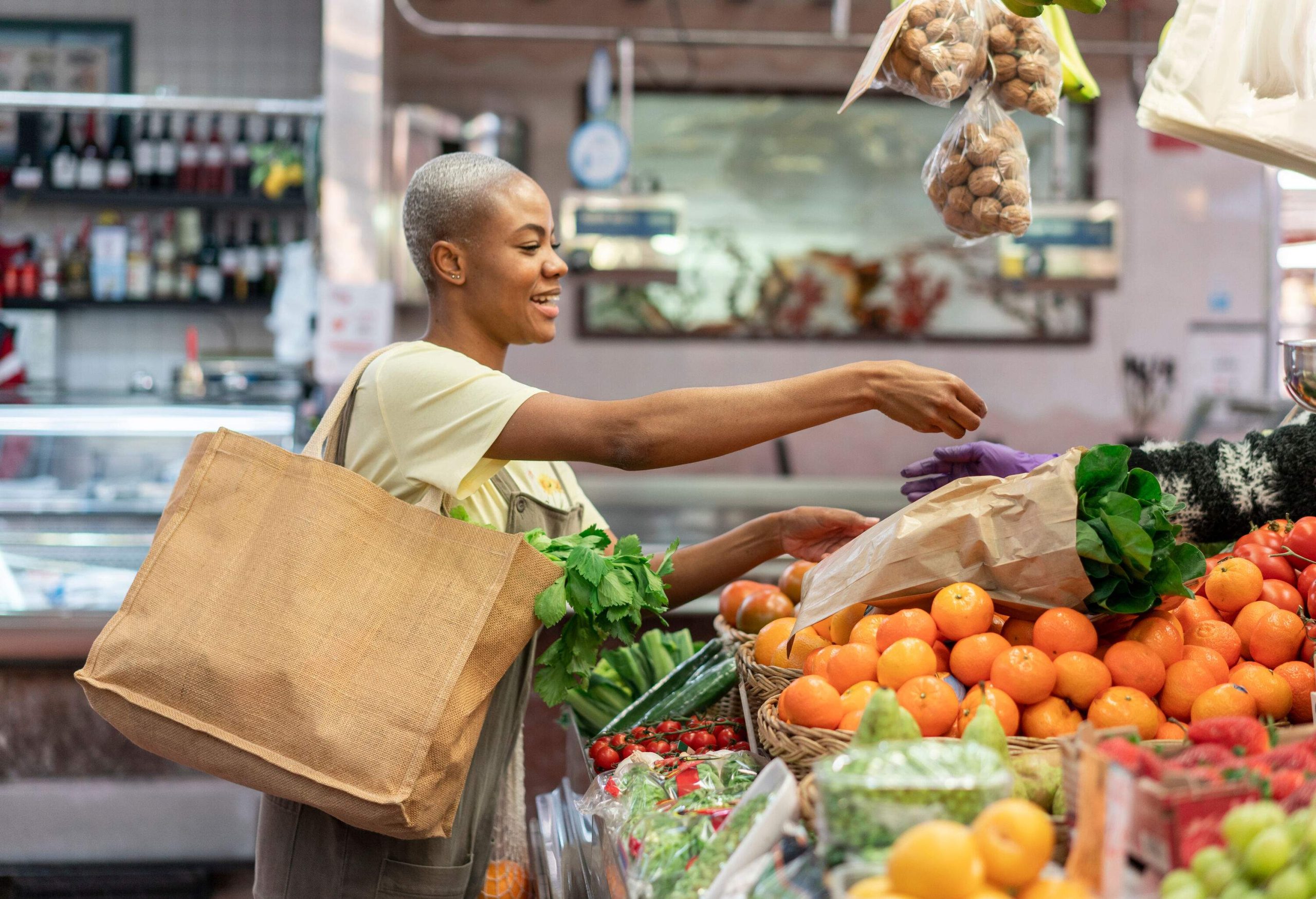 A bald woman buys some green leafy vegetables on a stall in a covered market.