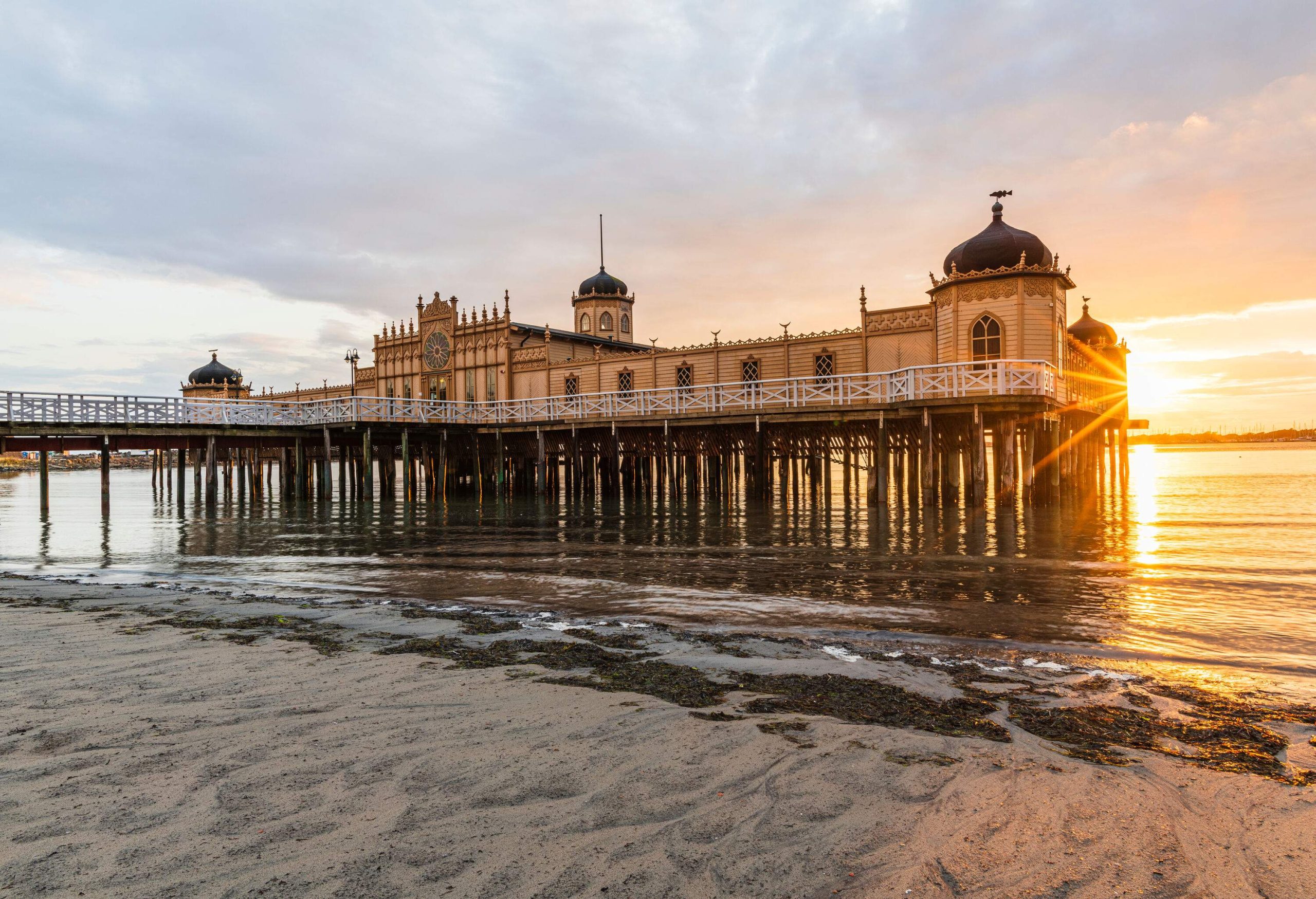 The Moorish-inspired Varbergs Kallbadhus is a bathhouse on stilts located on a beach with the sun shining behind it.