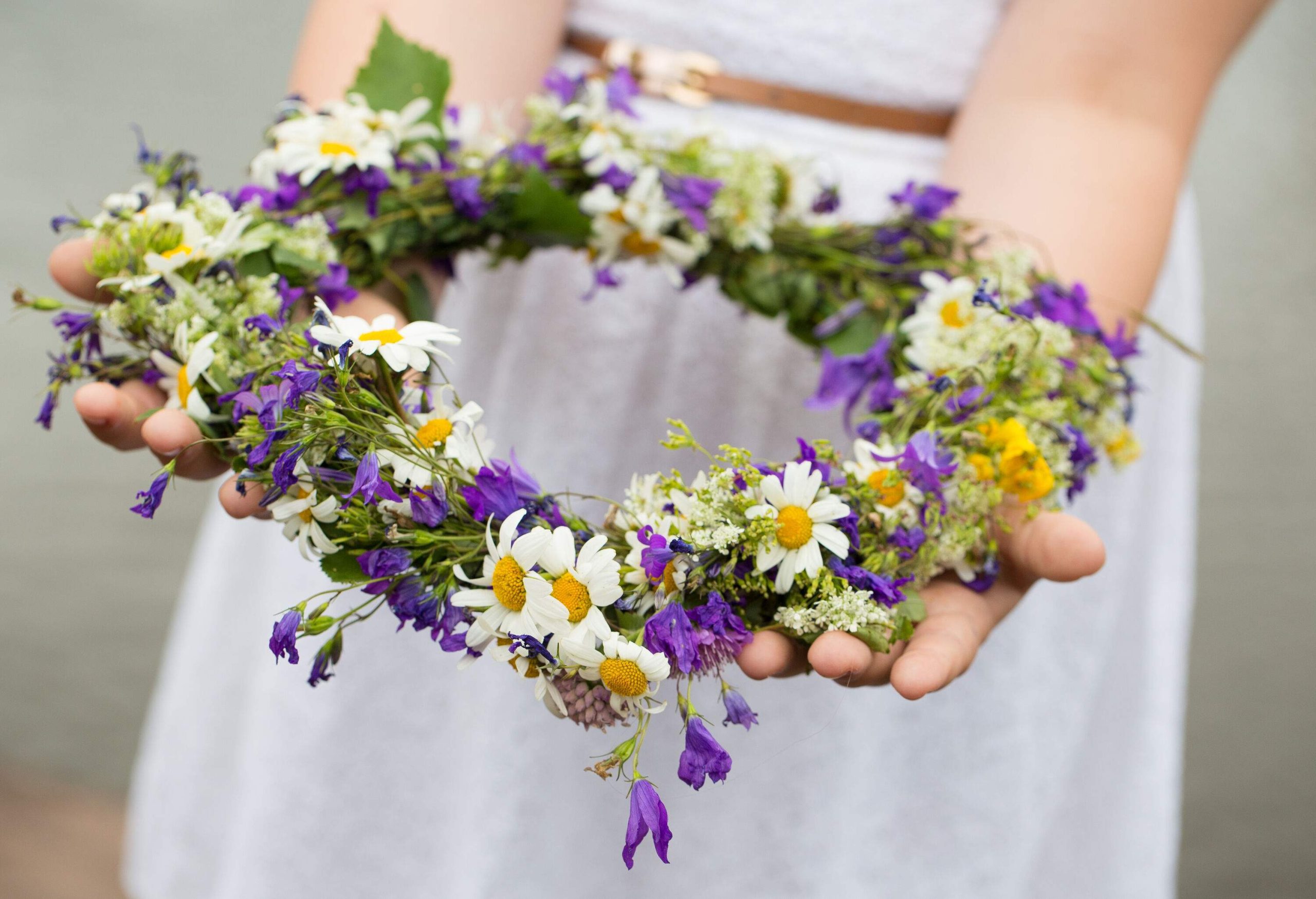 A child holding a headdress made of leaves and colourful flowers.