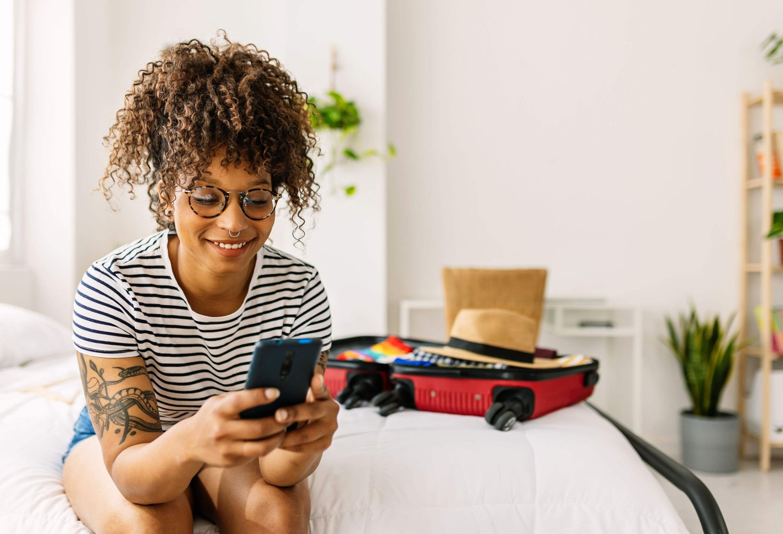 Happy young african american woman booking a hotel room while packing her summer suitcase for holidays