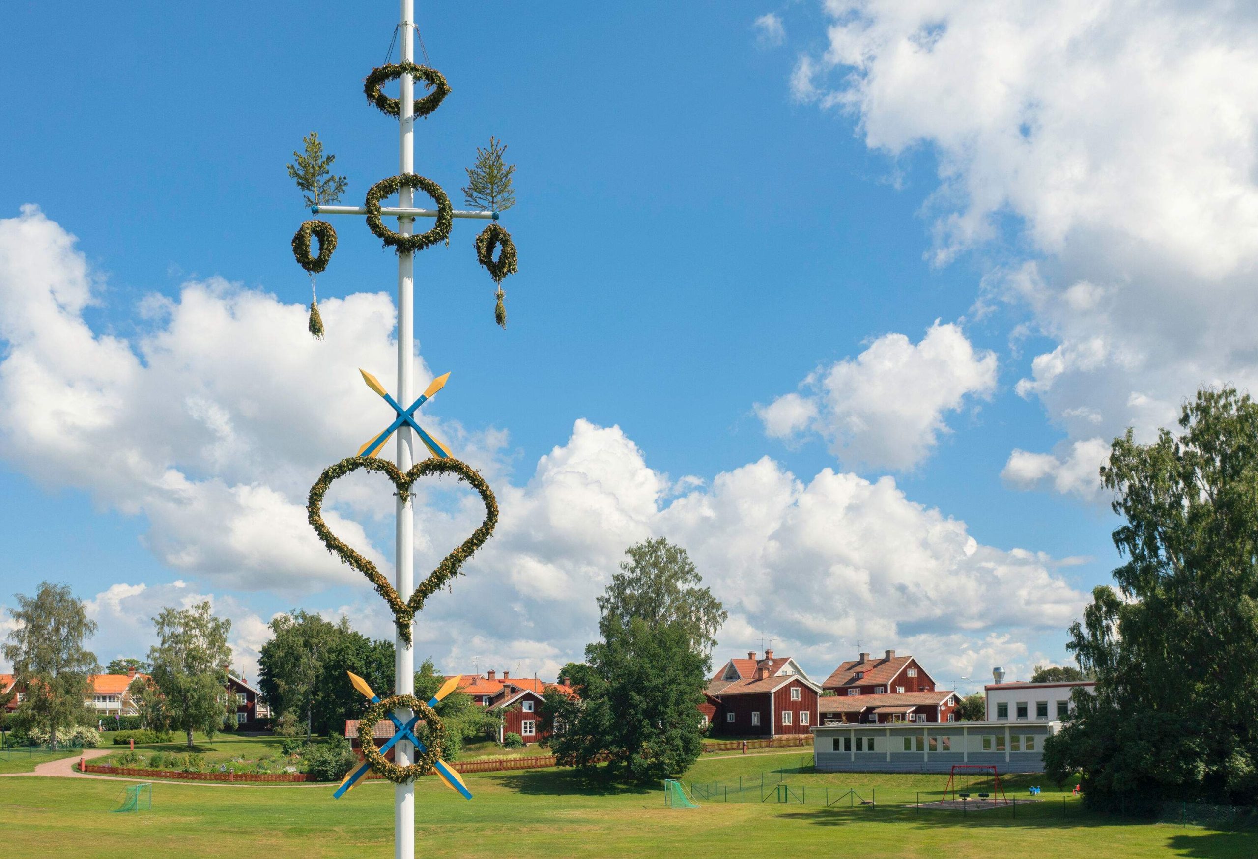 A white pole decorated with heart and circle flower garlands in a green park.